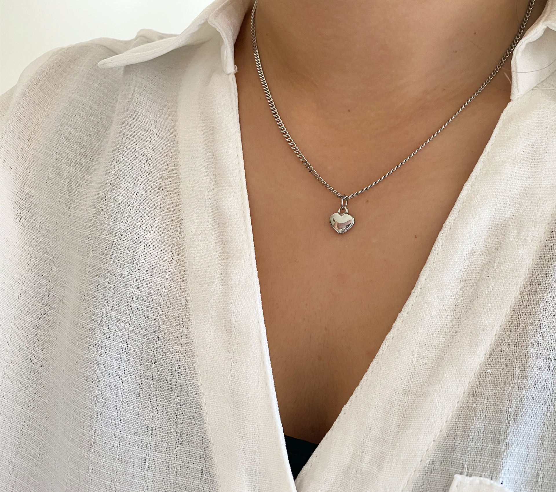 Colar prateado com pendente de coração usado por pessoa com camisa branca