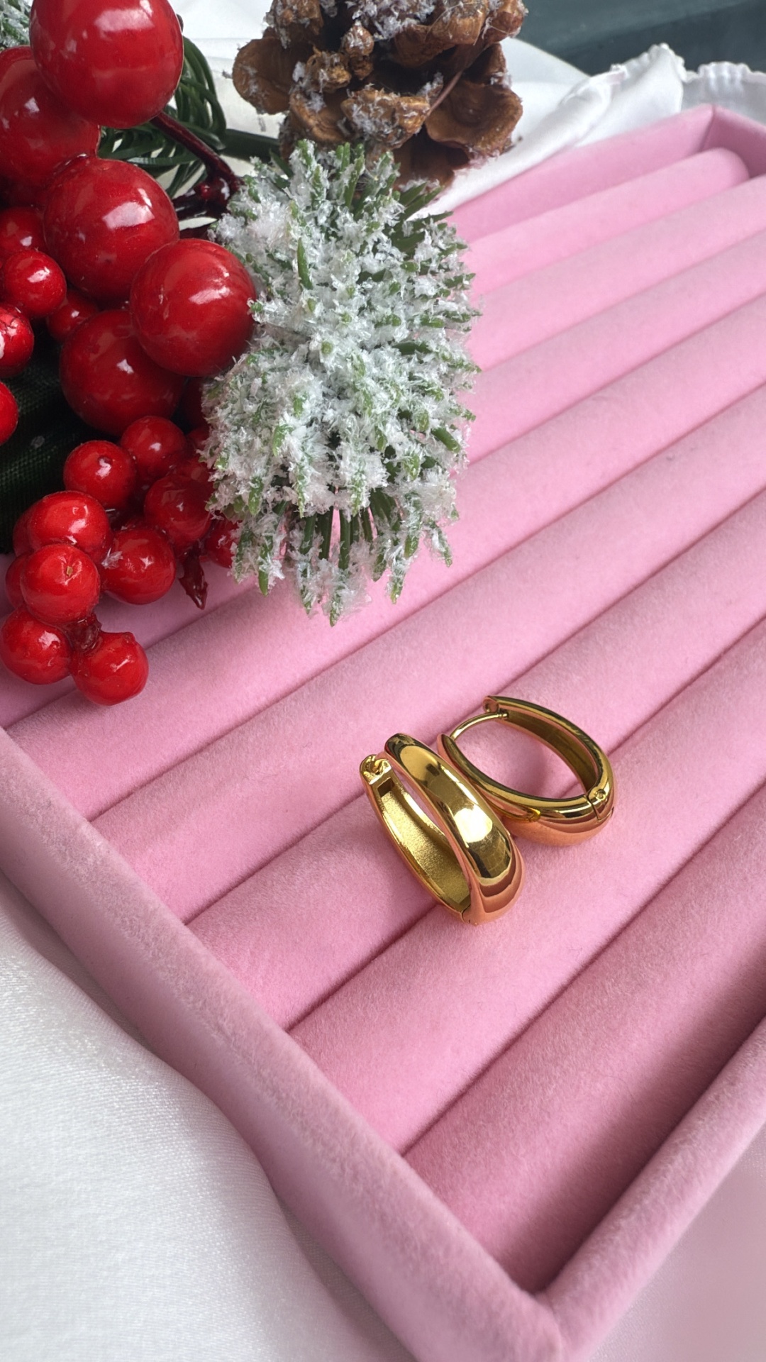 Brincos dourados ovalados em caixa rosa com decoração de raminho festivo