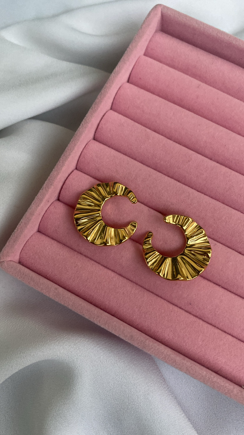 Brincos dourados com textura ondulada numa caixa rosa de veludo