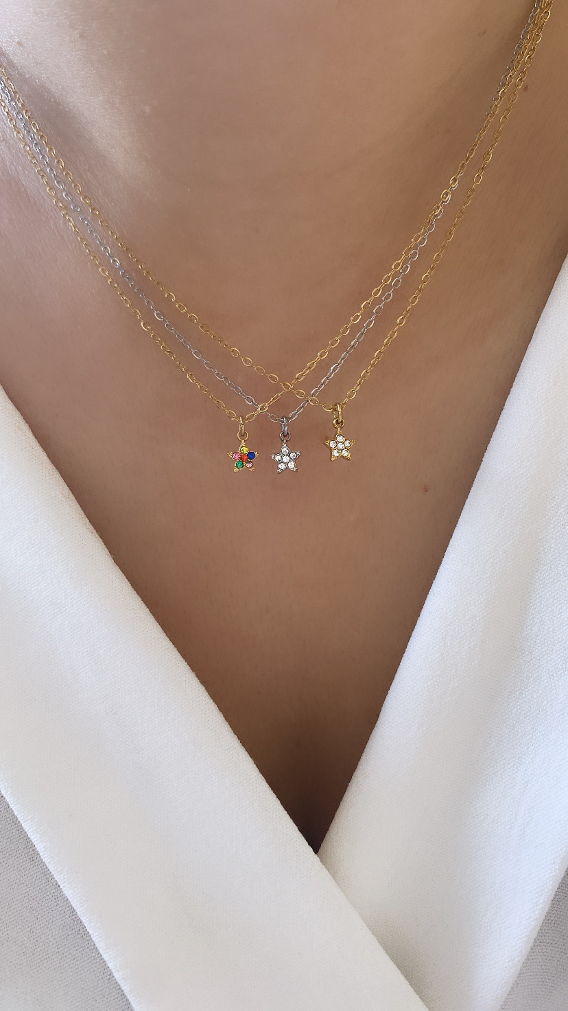 Três colares finos com pendentes em forma de flor, dois dourados e um prateado, em decote branco.