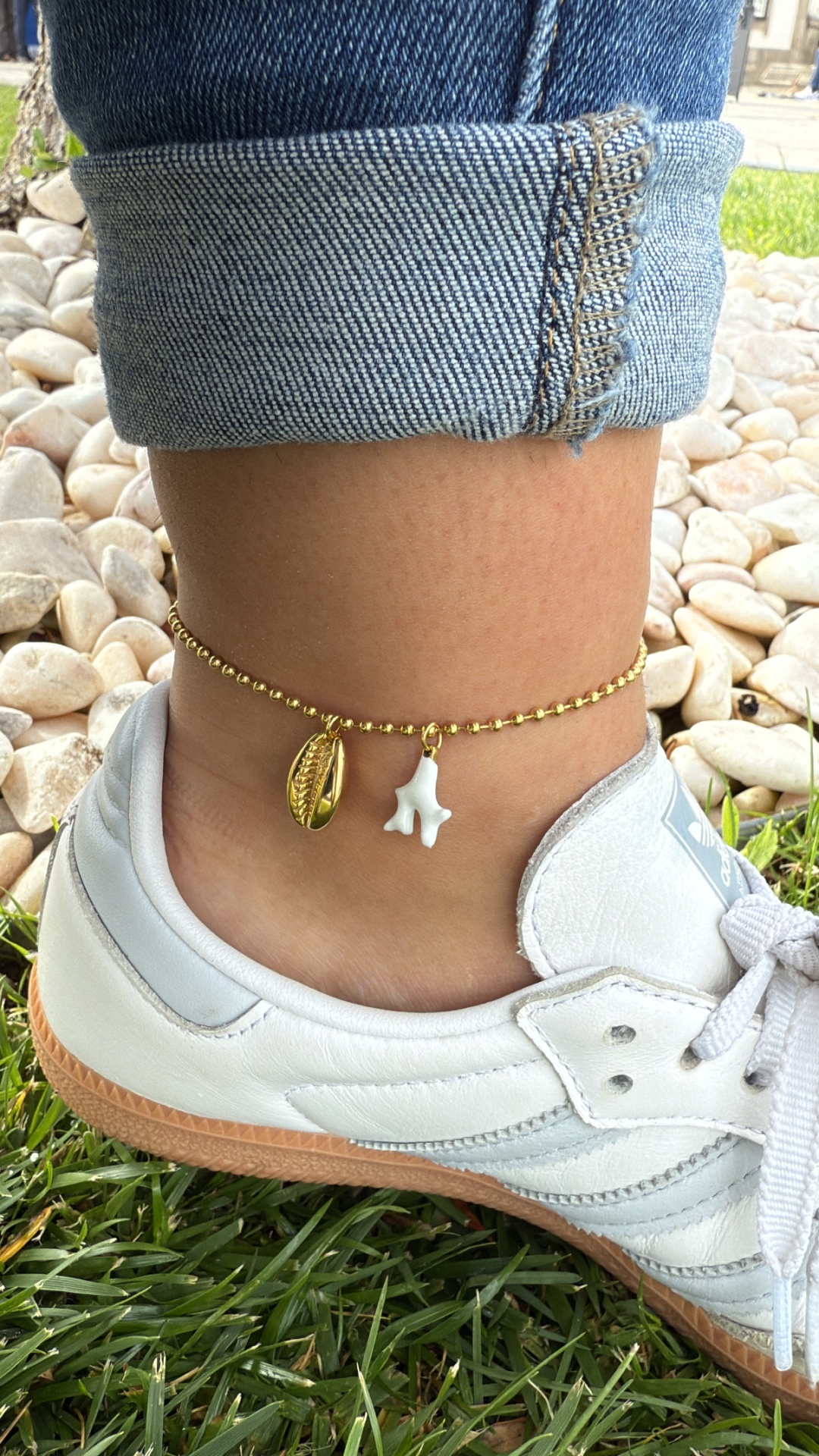 Tornozeleira dourada com pingentes em torno de tornozelo com jeans e ténis brancos