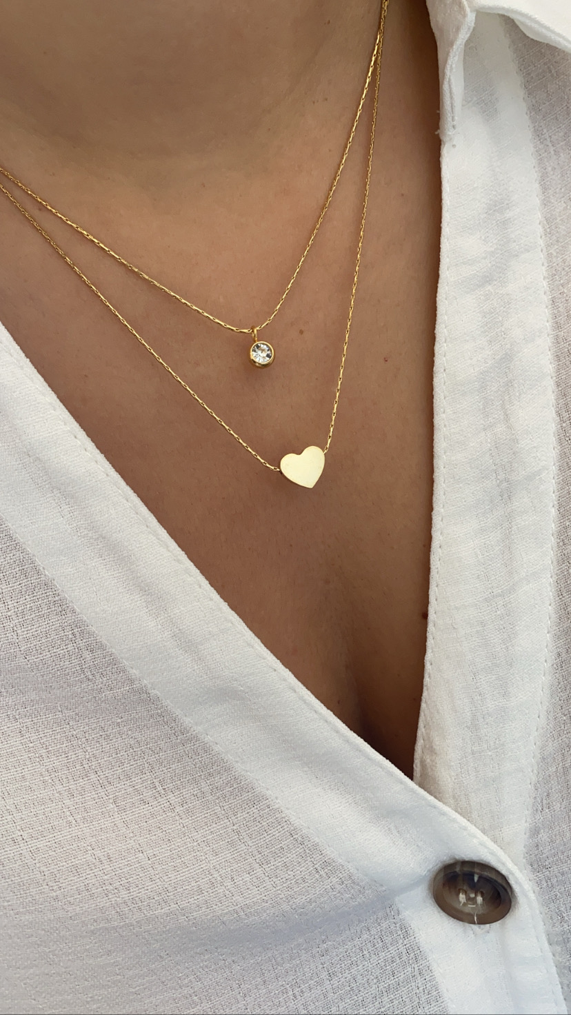 Colar duplo em ouro com pendentes de círculo e coração, camisa branca com botão castanho
