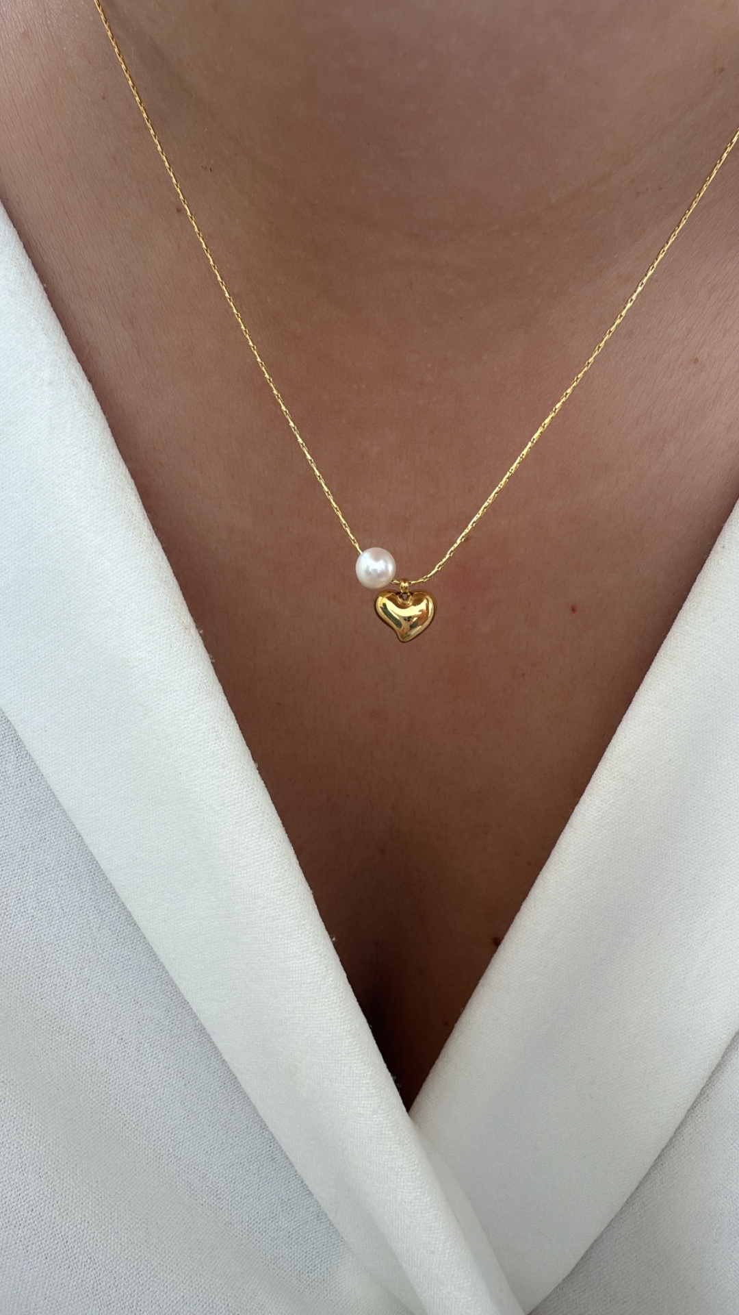 Colar dourado com coração e pérola sobre blusa branca