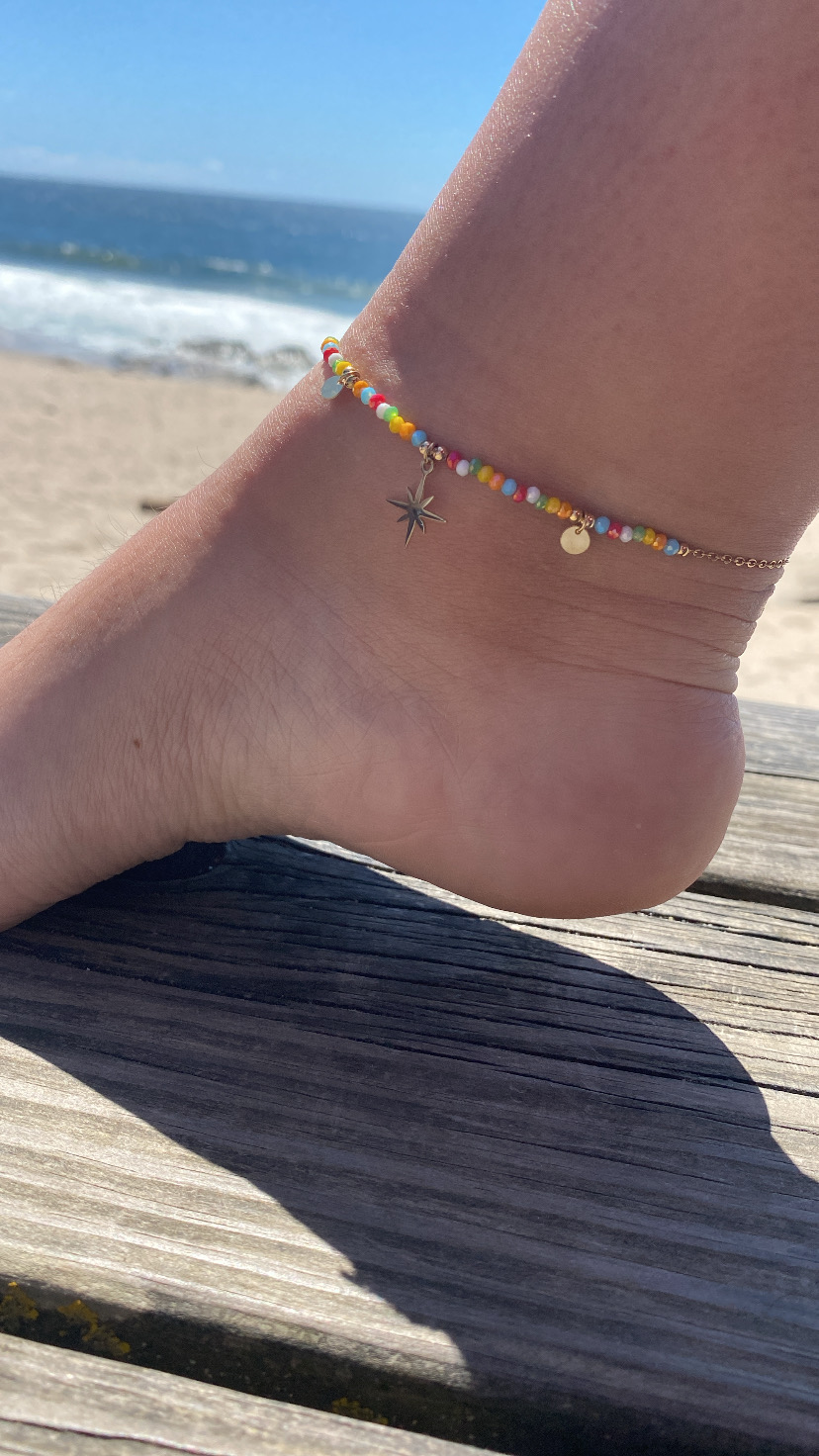 Pulseira de tornozelo colorida com pendentes metálicos na praia