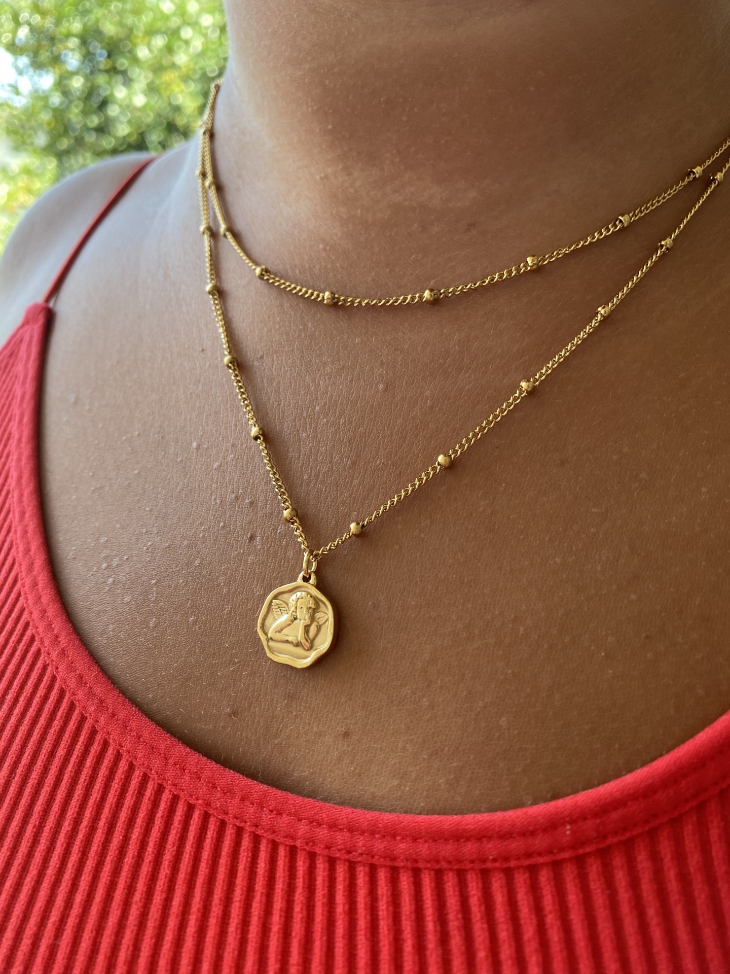 Colar dourado com medalhão em pessoa com camisola vermelha canelada.