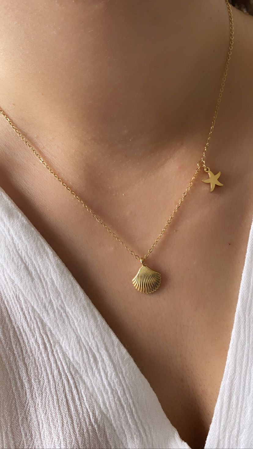 Colar dourado com pendentes de concha e estrela-do-mar em pescoço com blusa branca