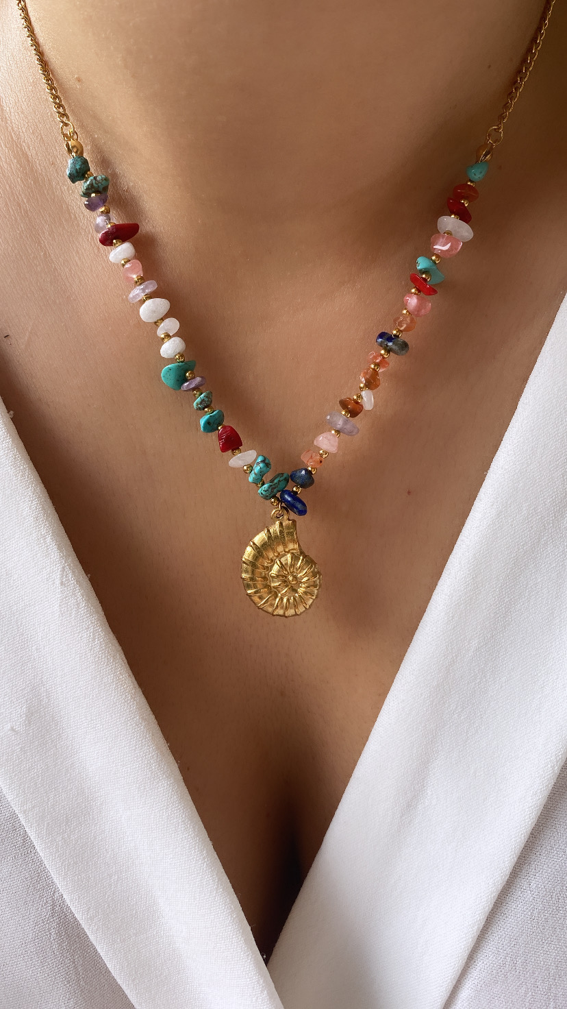 Colar com pedras coloridas e pendente dourado em forma de espiral sobre pele clara e vestido branco