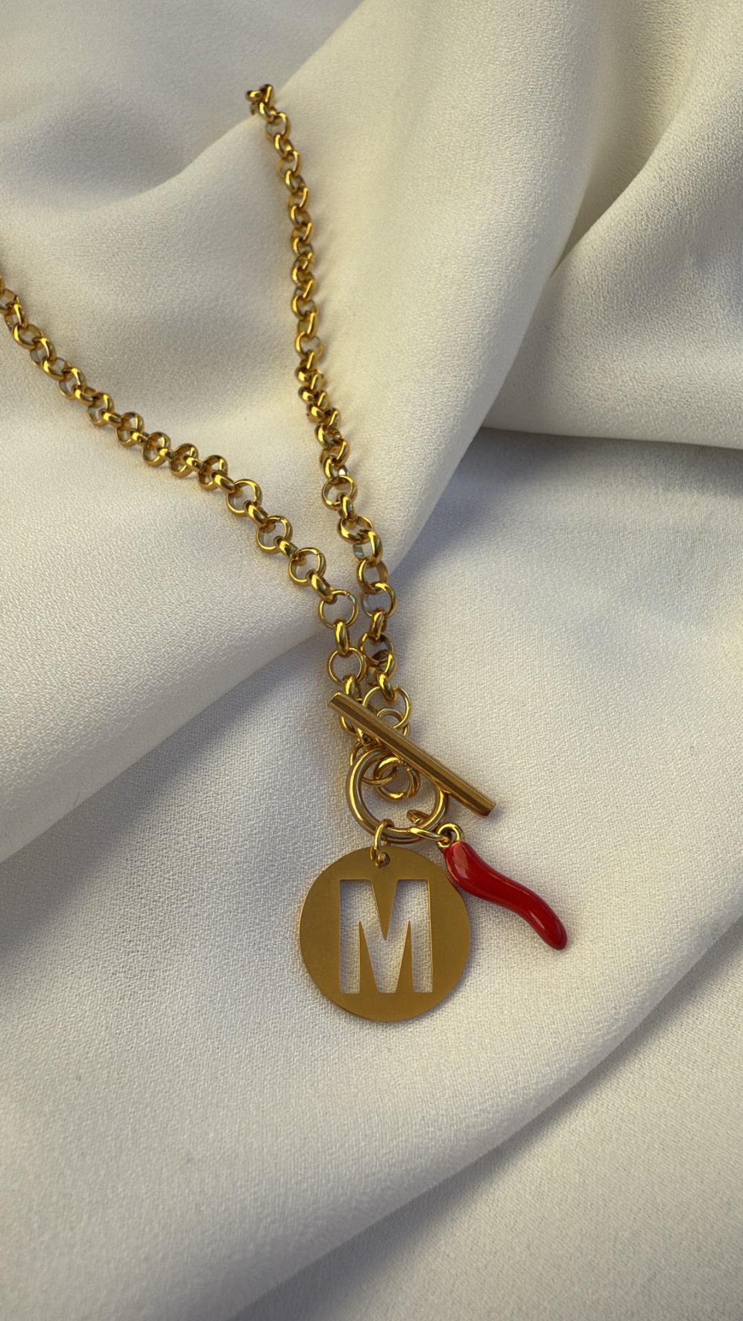 Colar dourado com pendente de letra M e pimenta vermelha