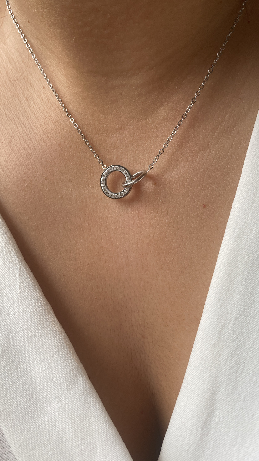 Colar prateado com pendente circular com pequenos brilhos num pescoço