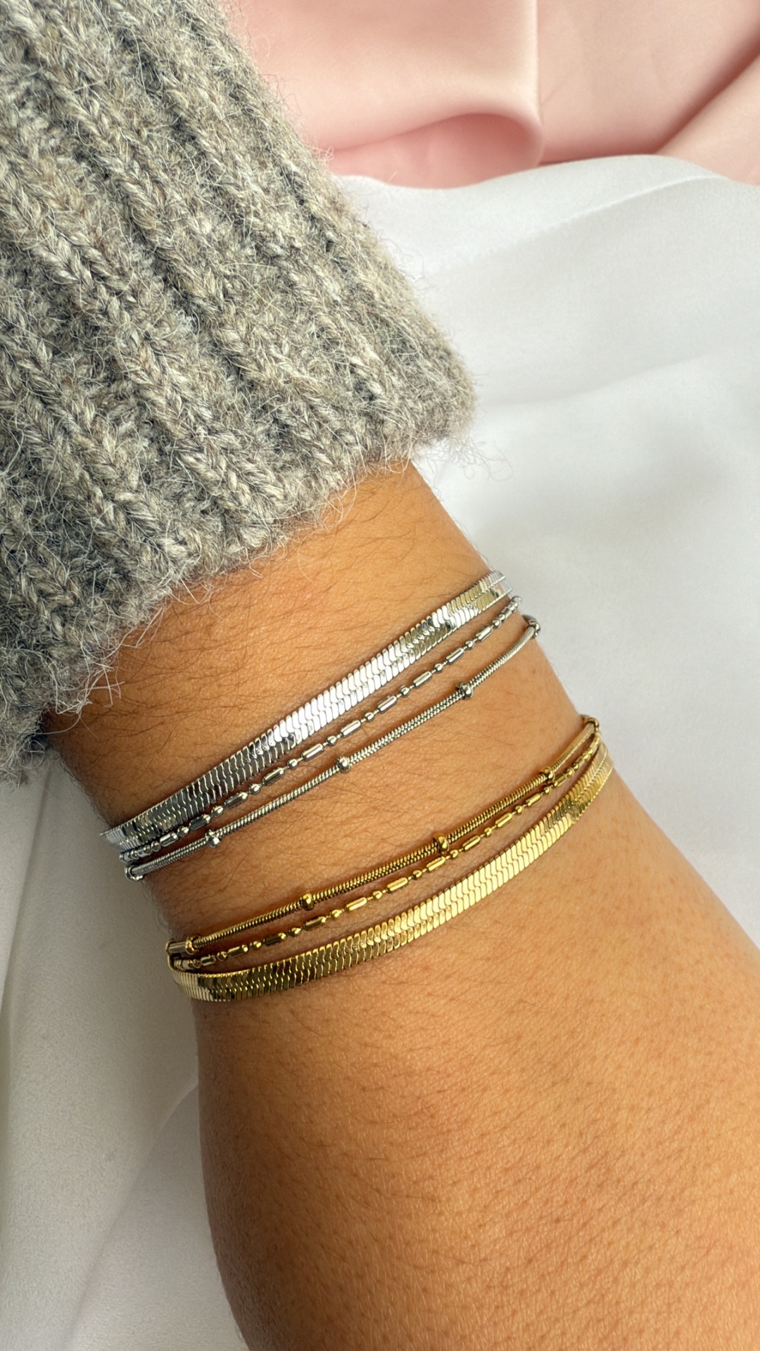 Conjunto de pulseiras finas prateadas e douradas no pulso de mulher com camisola cinza
