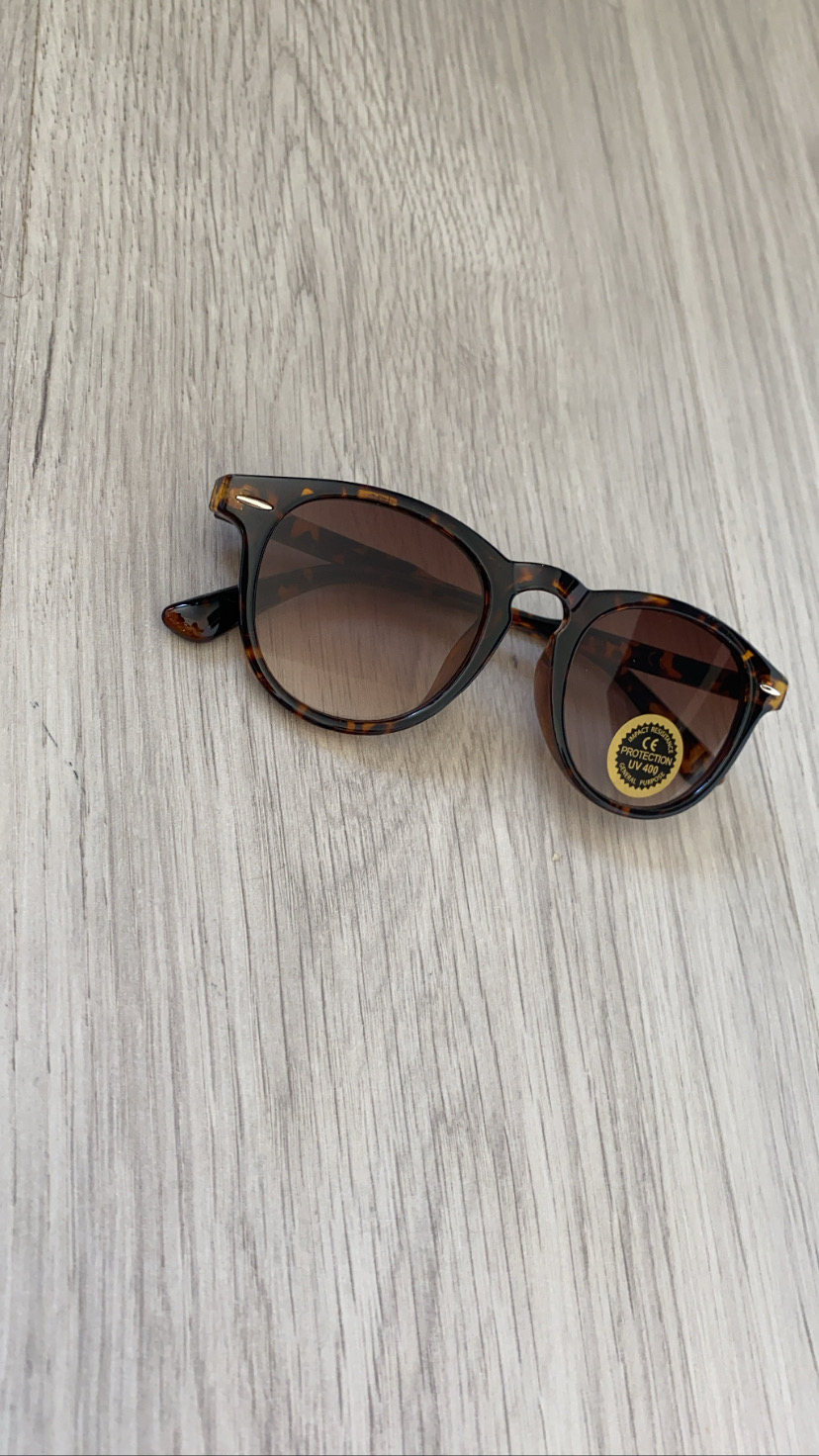Óculos de sol com armação tartaruga e lentes castanhas sobre madeira clara