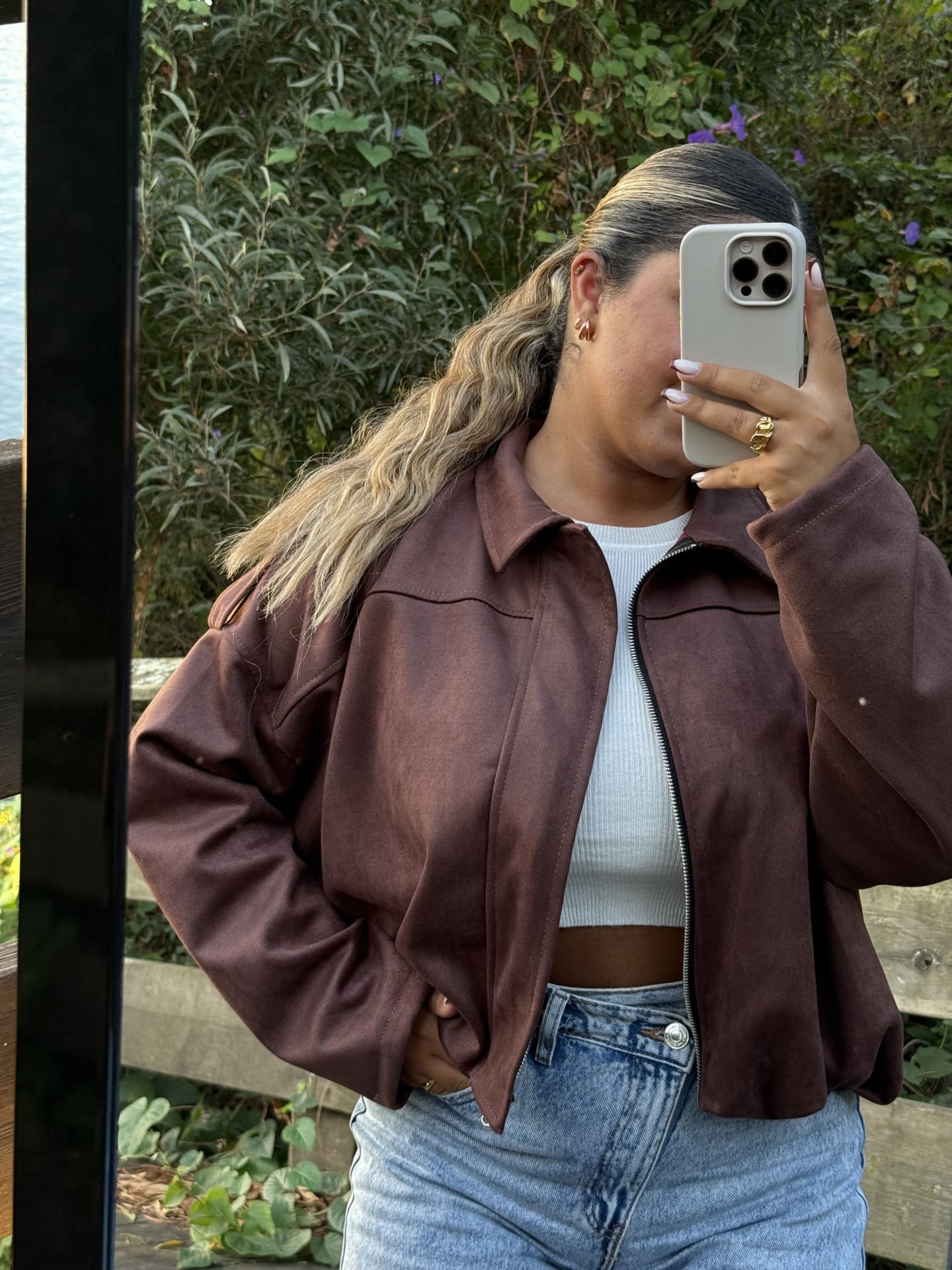 casaco castanho curto com top branco e calças de ganga, em ambiente exterior