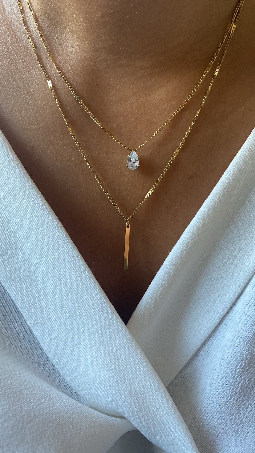 Colares duplos dourados com pendentes de gota e retângulo em pele com camisa branca