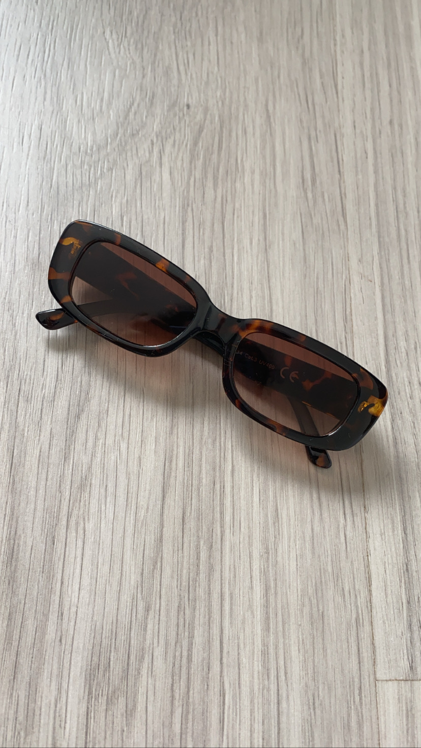Óculos de sol retangulares com padrão tartaruga castanho e lentes escuras sobre madeira clara