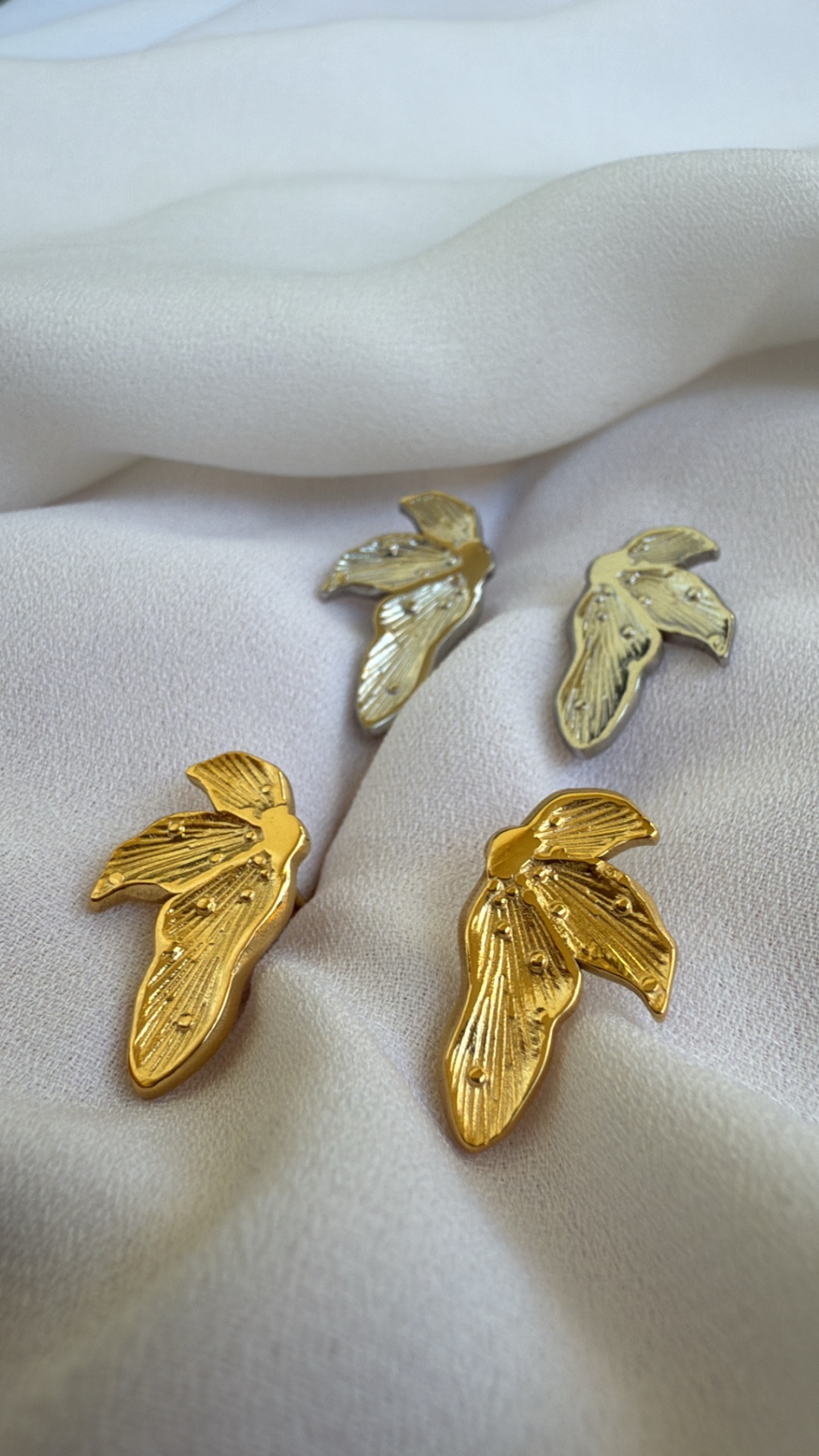 brincos em forma de folha dourados e prateados sobre tecido branco