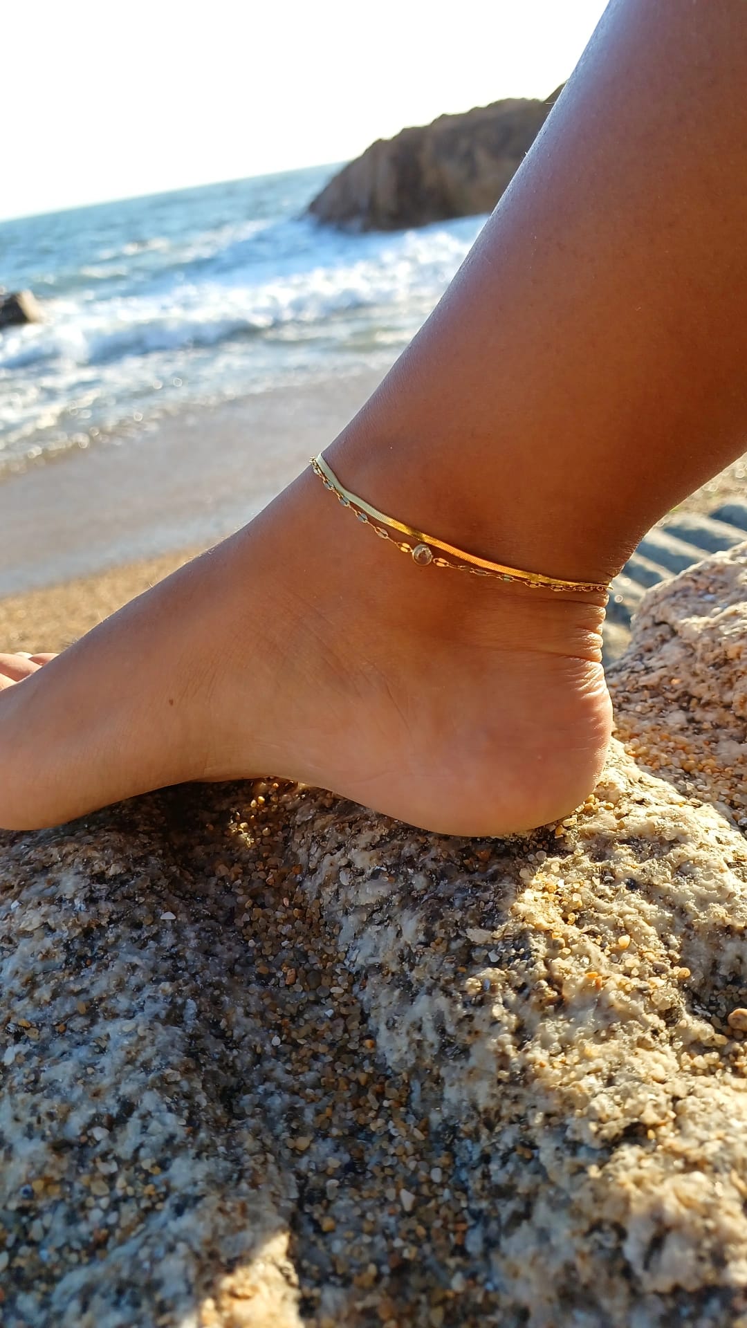 Tornozeleira dourada num tornozelo sobre rochas na praia