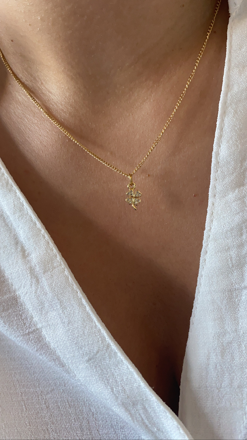 Colar dourado com pendente em formato de folha no pescoço de pessoa vestindo camisa branca