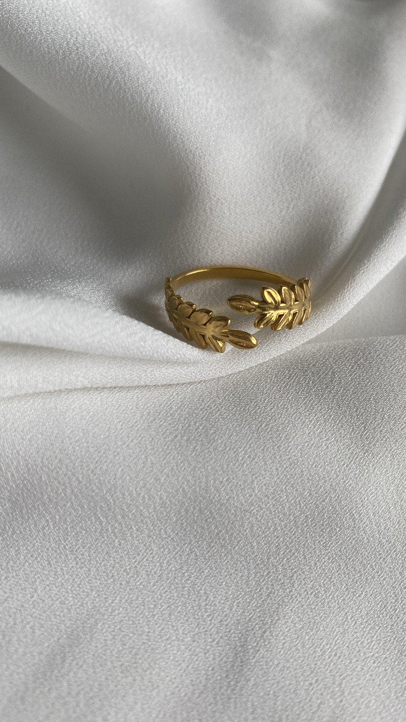 Anel dourado com design de folhas sobre tecido branco