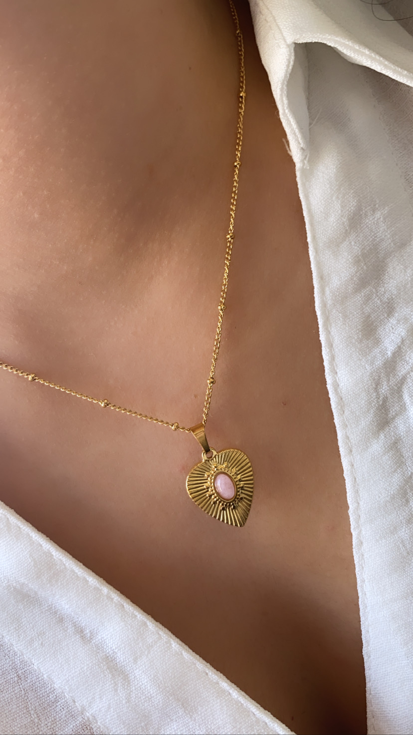 Colar dourado com pendente em formato de coração com pedra rosa, camisa branca