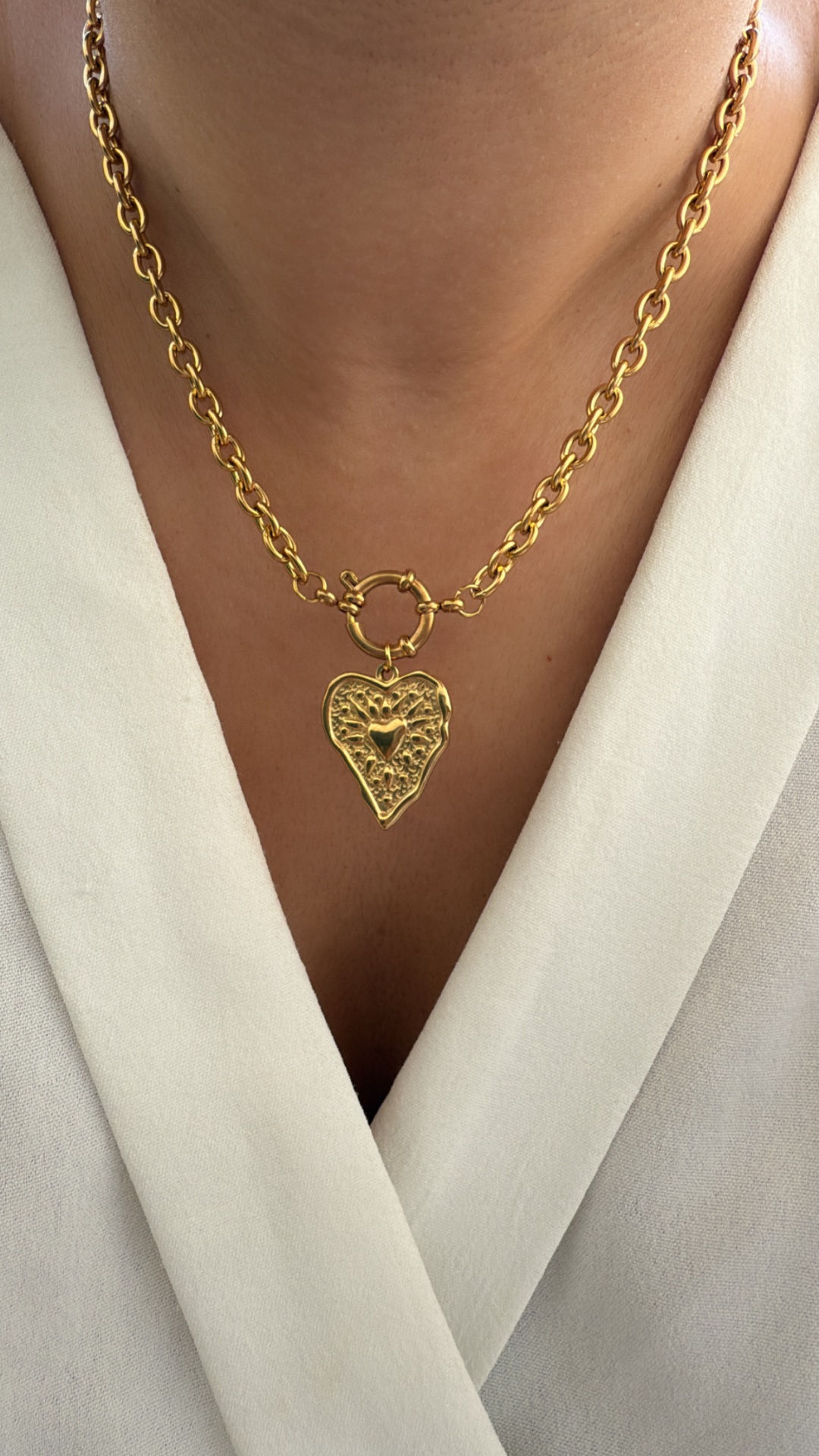 Colar dourado com pendente de coração texturizado sobre camisa branca
