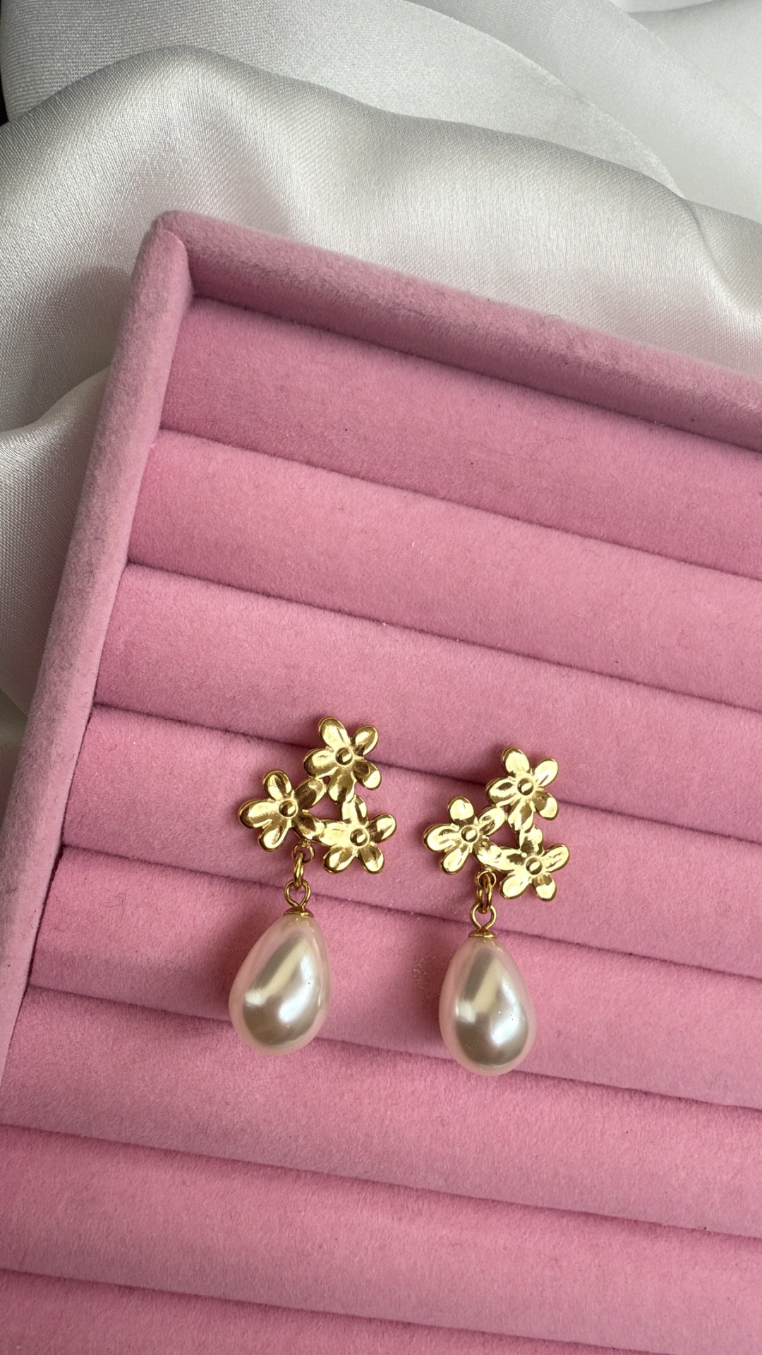 Brincos dourados com flores e gotas de pérola num suporte rosa