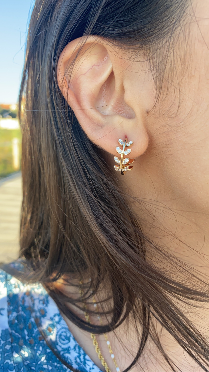 Brinco em metal dourado com folhas e pedras brilhantes numa orelha de mulher