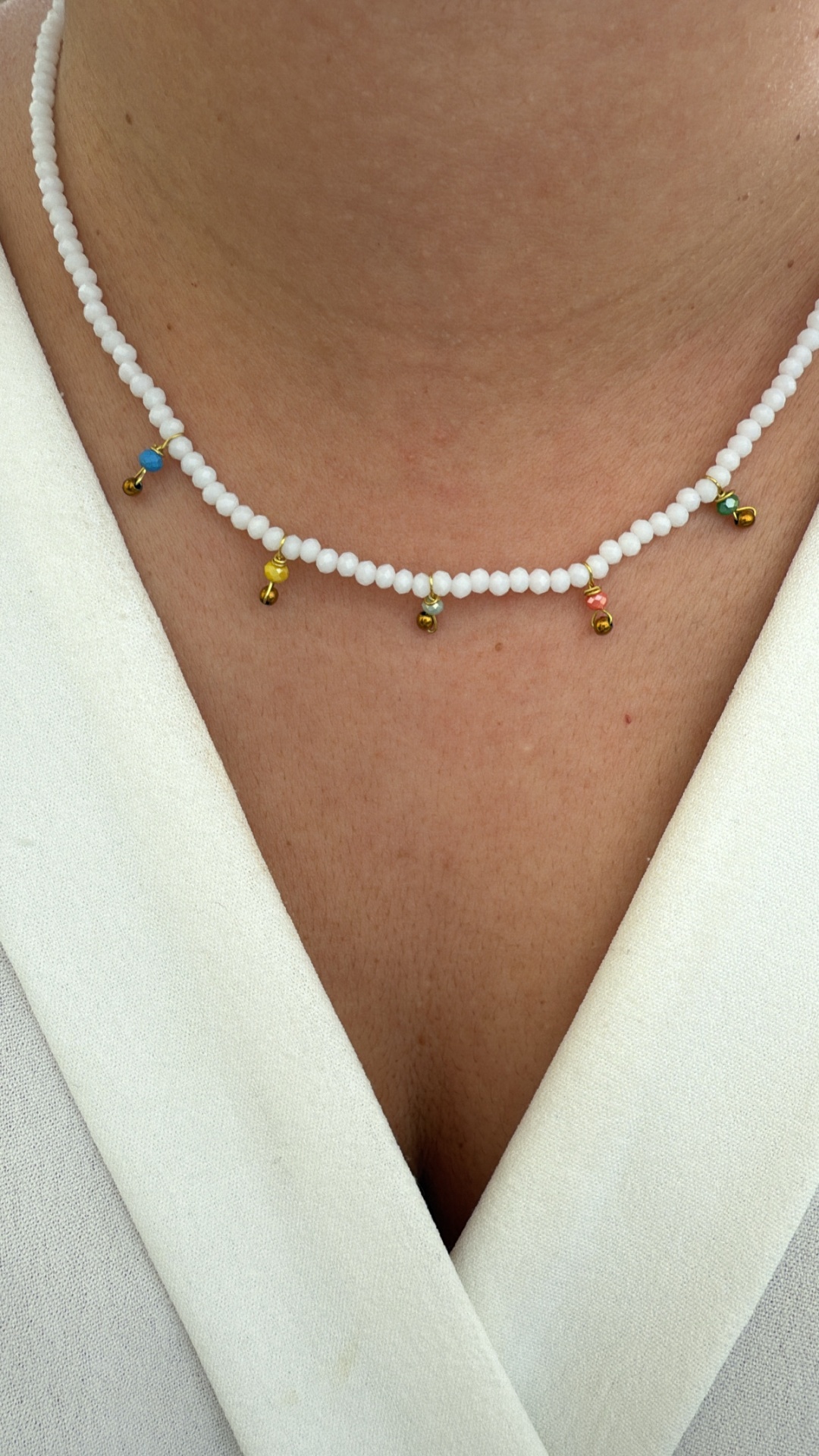 Colar de contas brancas com pendentes coloridos numa pessoa com camisa branca.