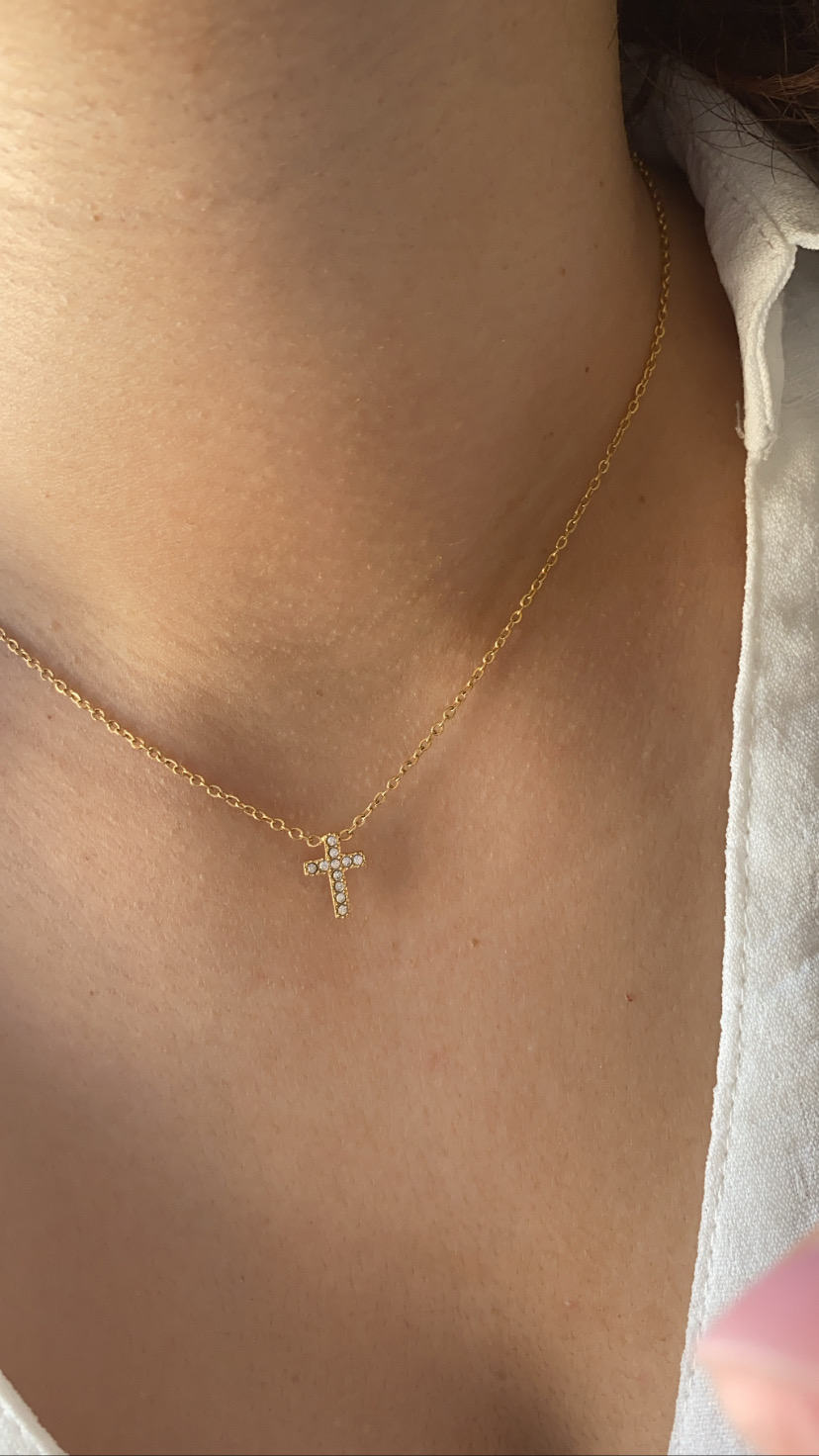 Colar dourado com pendente de cruz em pedras brilhantes no pescoço
