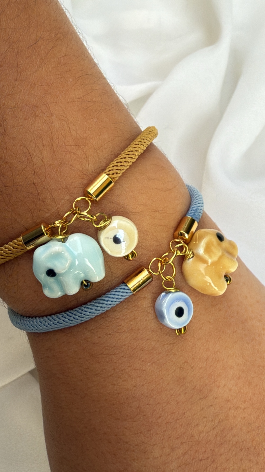 Duas pulseiras de fio trançado com pingentes de elefante em cerâmica e olhos gregos em vidro.