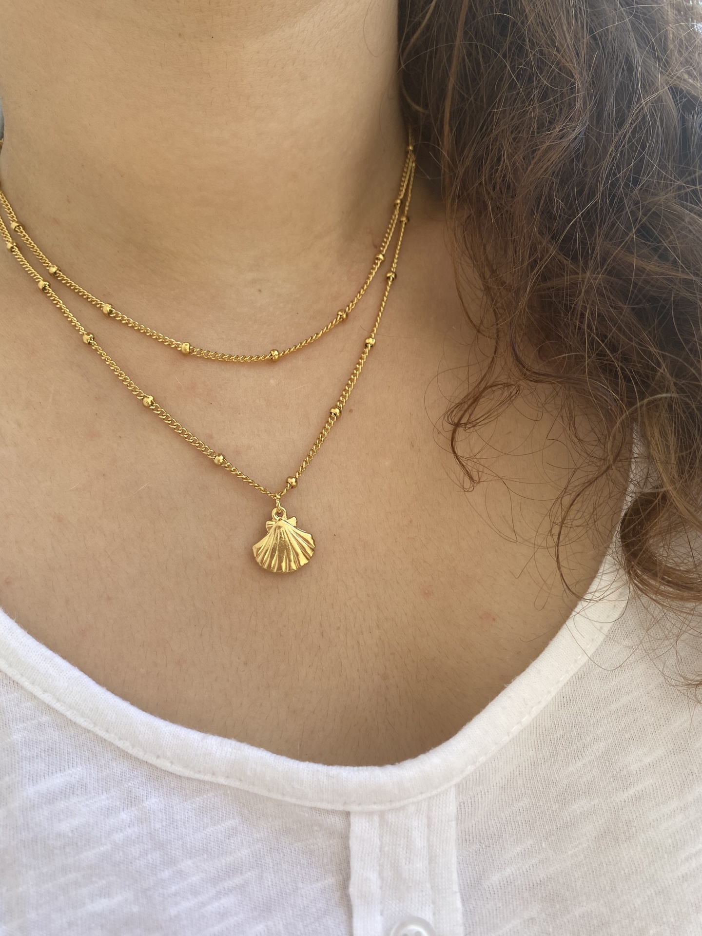 Colar duplo dourado com pendente de concha usado no pescoço