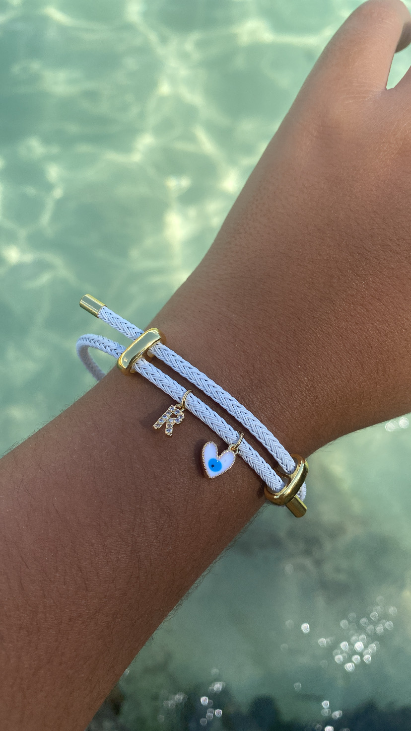 Pulseira branca com pendentes dourados e azul no pulso sobre fundo de água