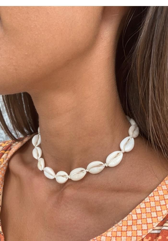 Gargantilha de conchas brancas naturais no pescoço de mulher com padrão laranja na roupa.