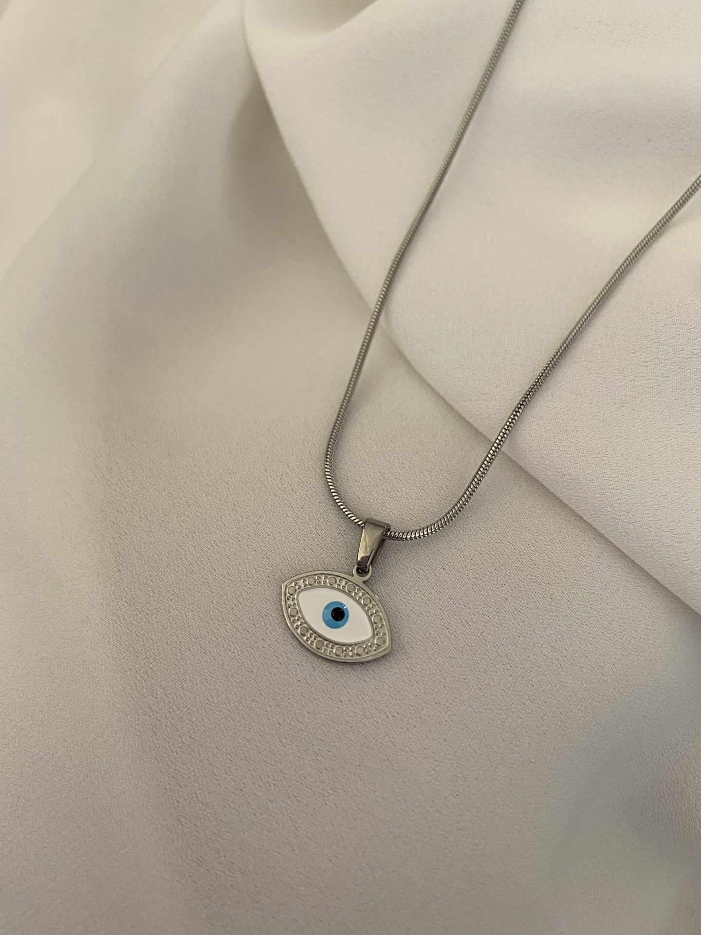 Colar prateado com pingente em forma de olho sobre tecido branco