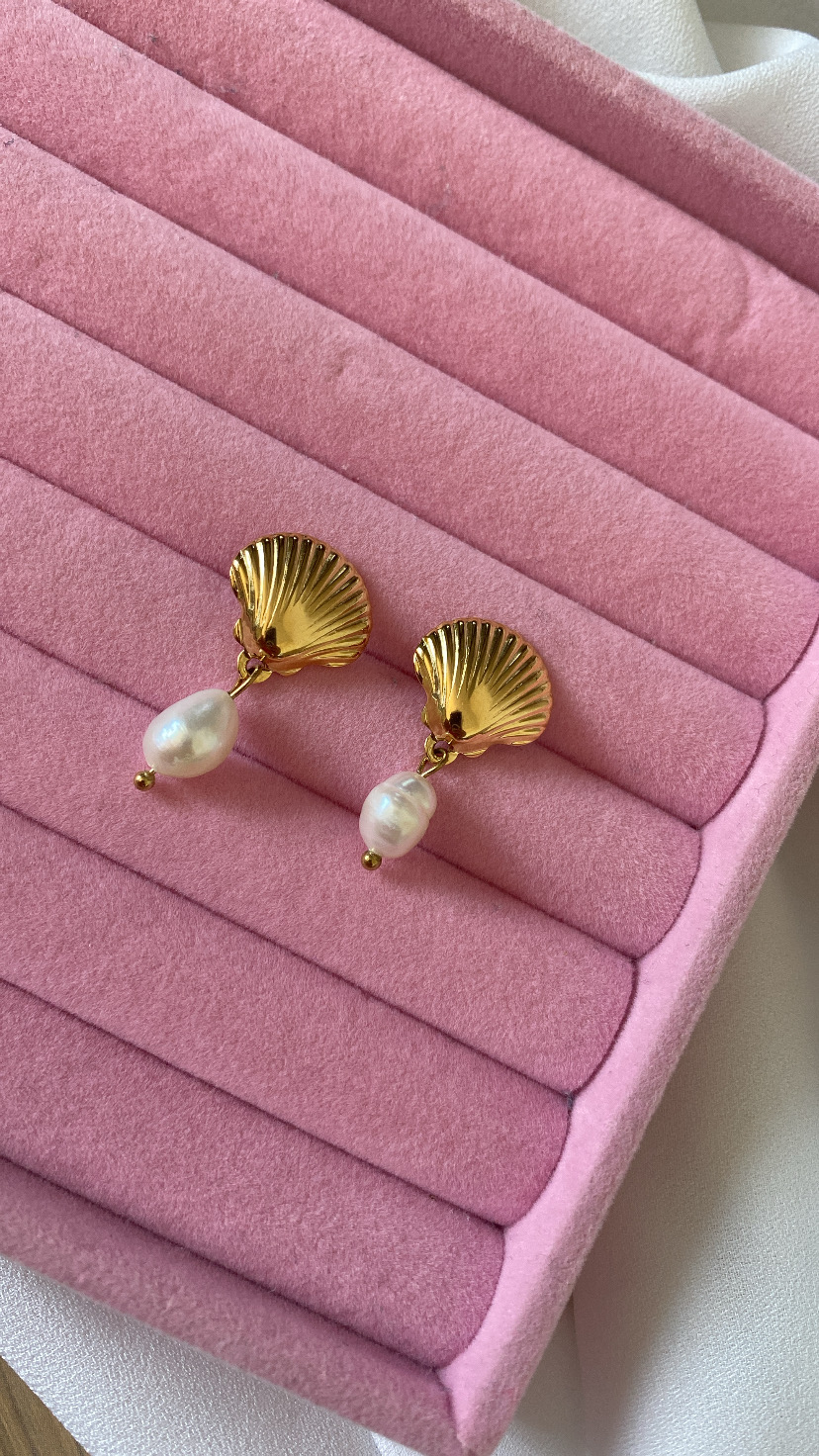 Brincos dourados em forma de concha com pérolas penduradas em suporte rosa aveludado