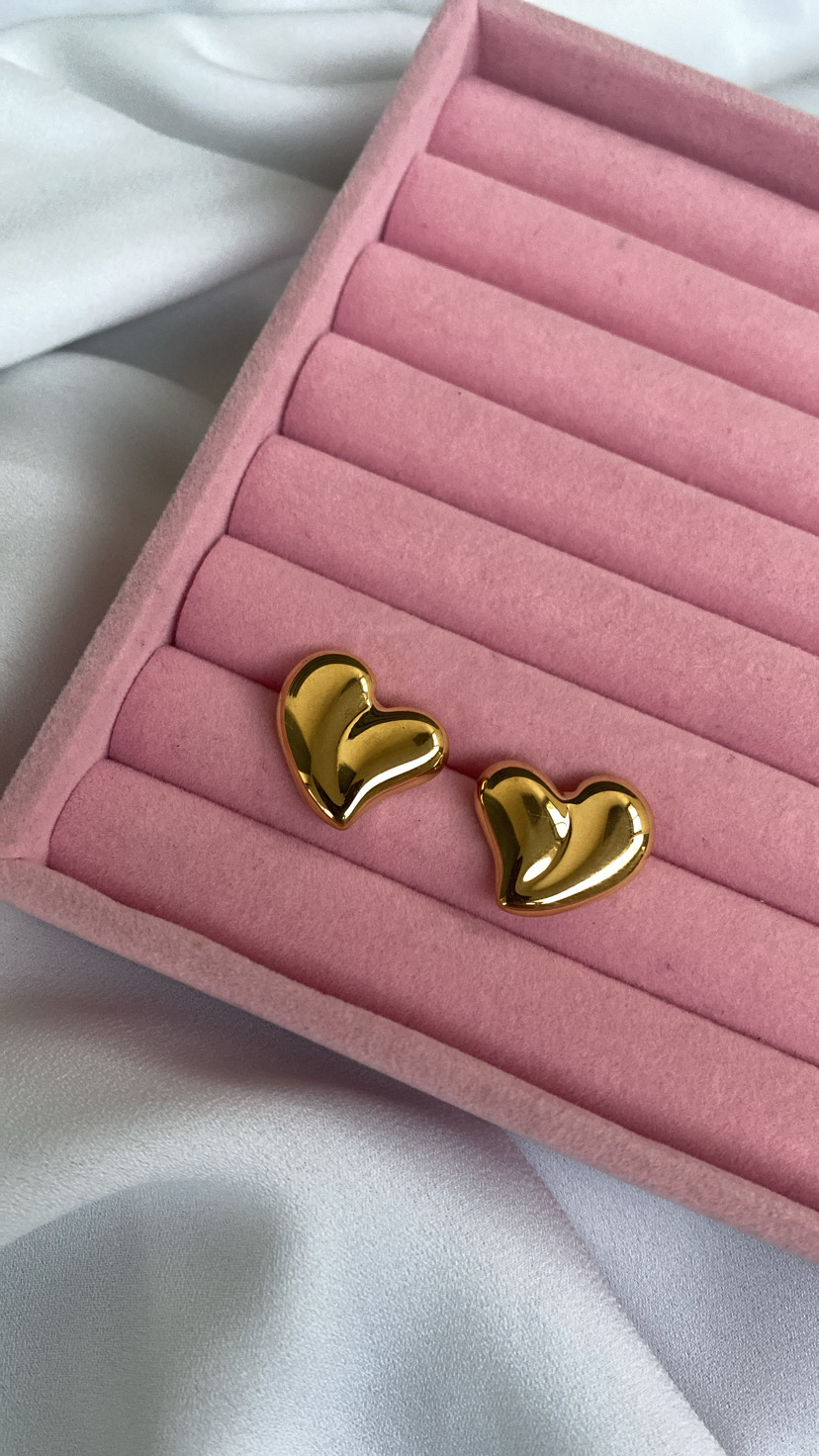 Brincos dourados em forma de coração sobre caixa rosa de veludo em tecido branco