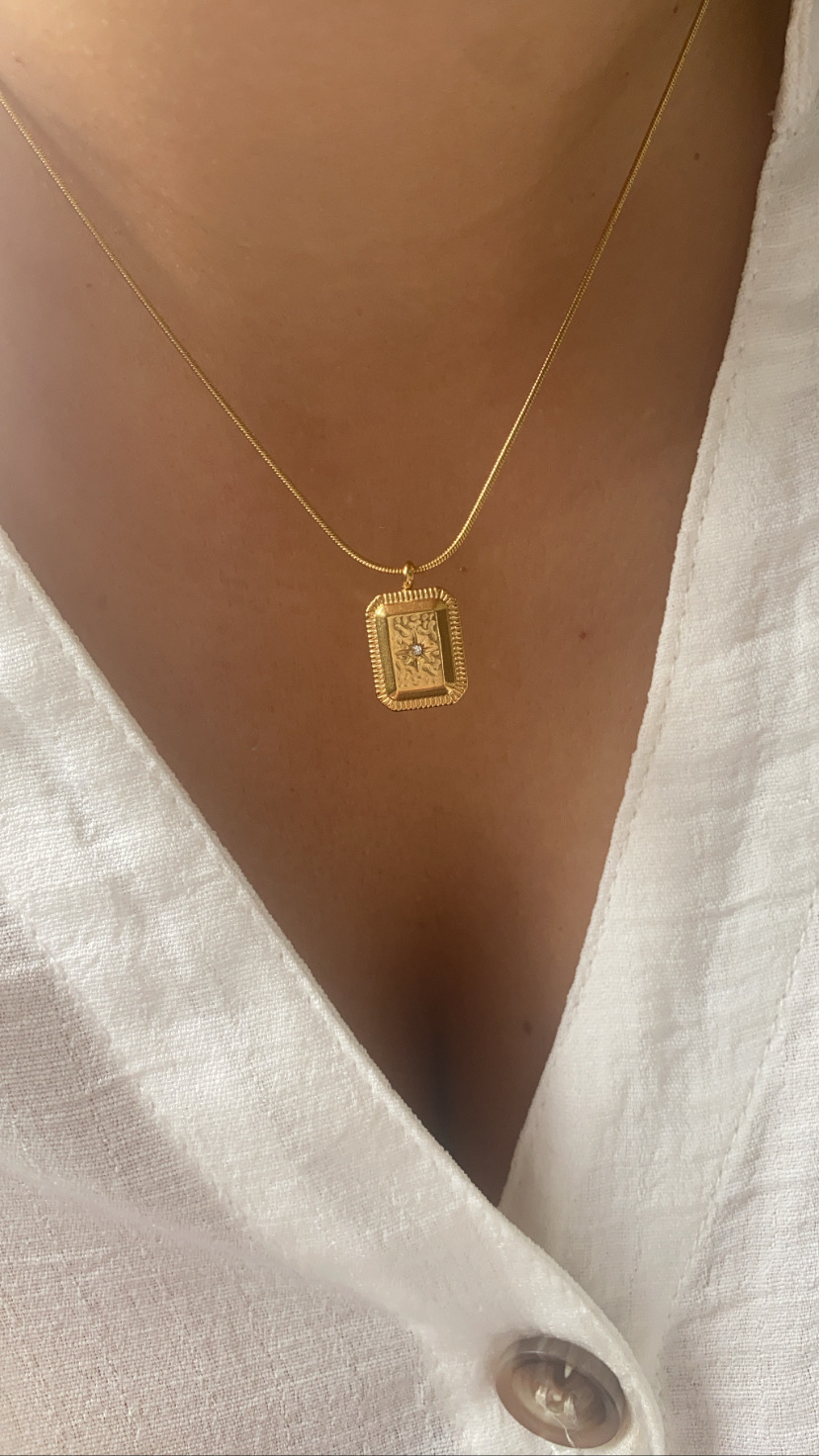 Colar dourado com pendente retangular usado com camisa branca