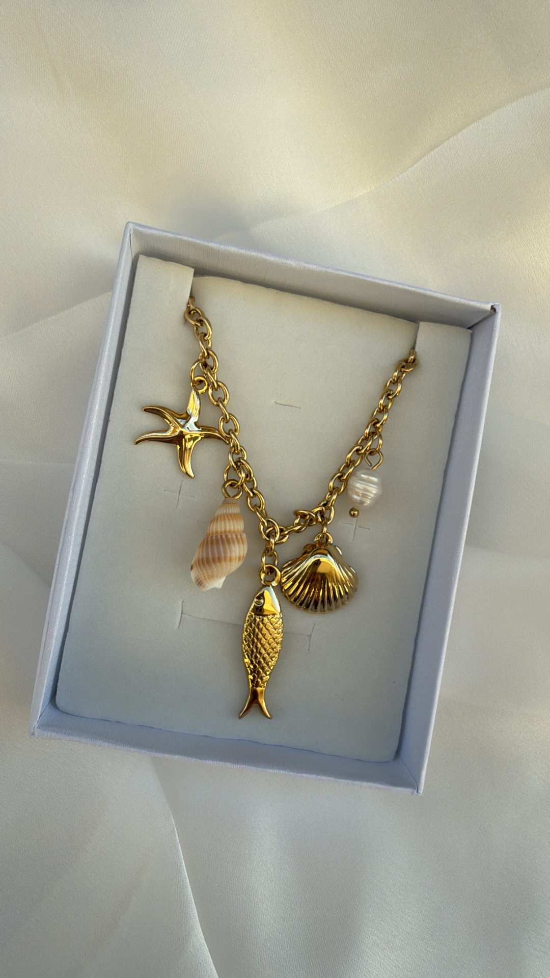 Colar dourado com pendentes marinhos numa caixa branca