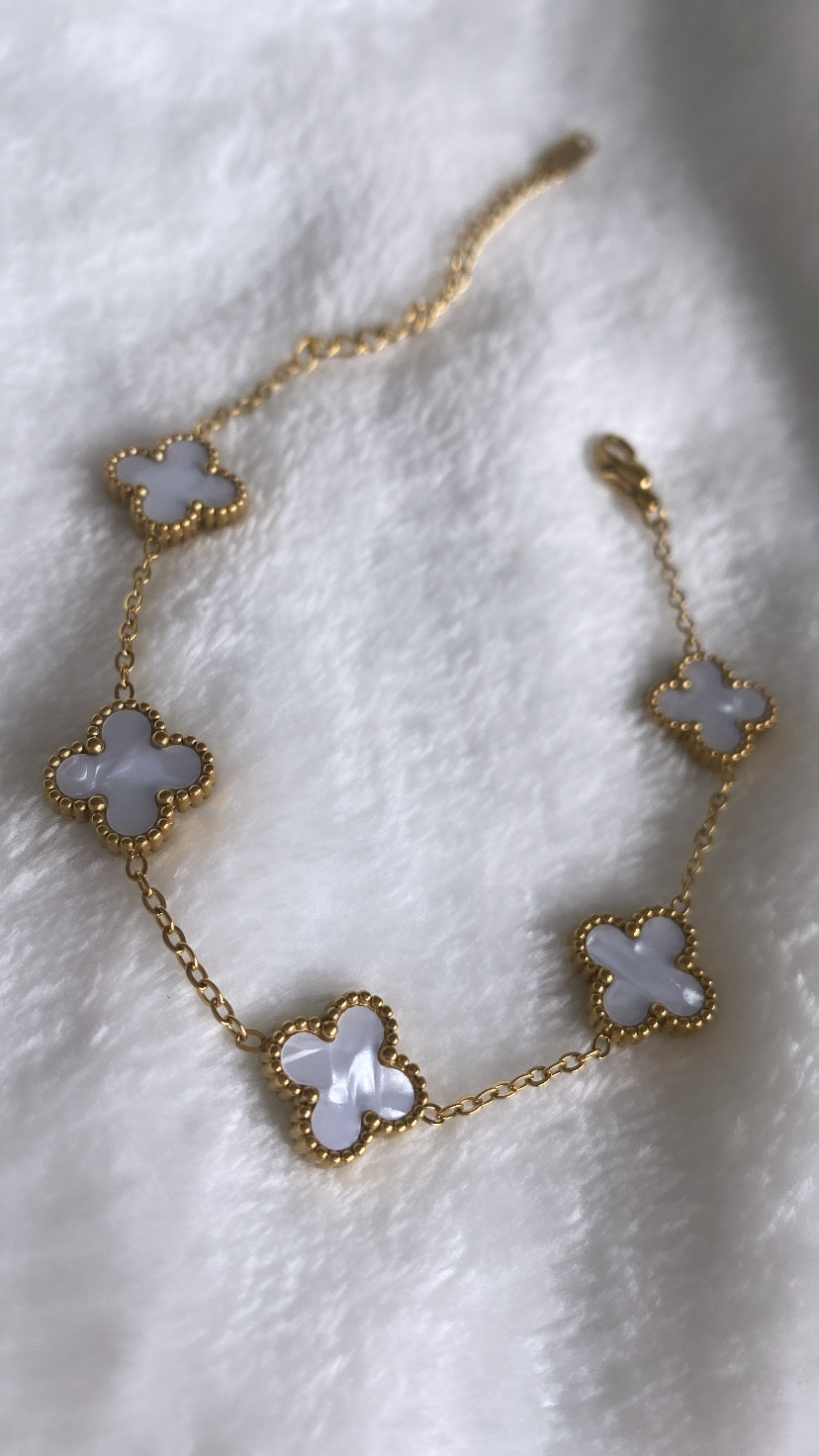 Pulseira dourada com pendentes em forma de trevo branco sobre tecido branco