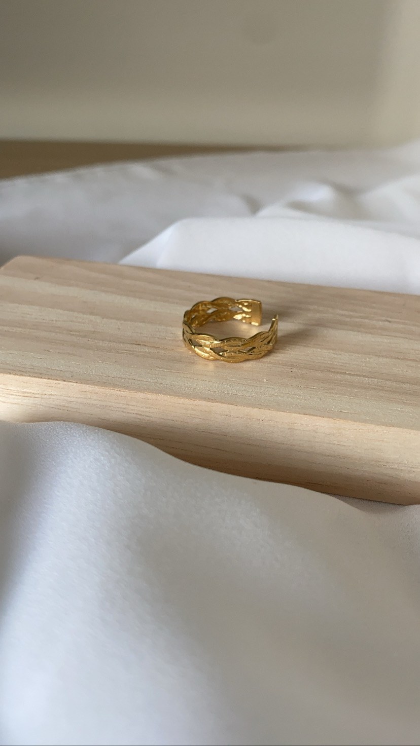 Anel dourado texturizado sobre base de madeira clara e fundo branco