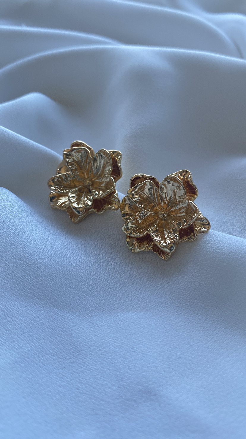 Brincos dourados em forma de flor sobre tecido branco