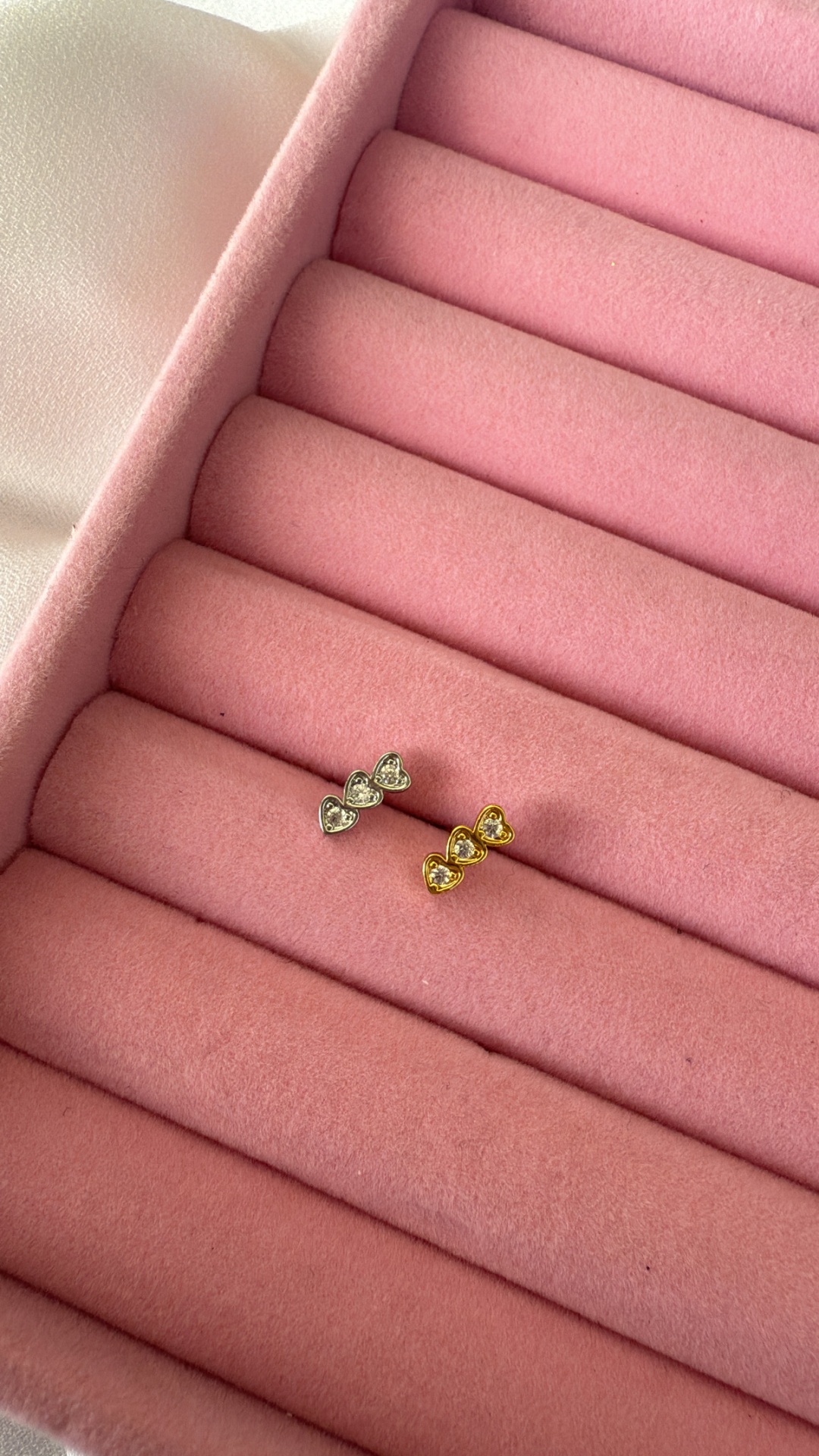 Brincos de corações em prata e dourado com pedras em suporte rosa de veludo.