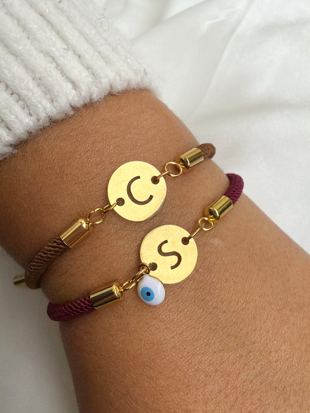 Pulseiras de corda com discos dourados e letras, uma com pendente olho turco, usadas no pulso