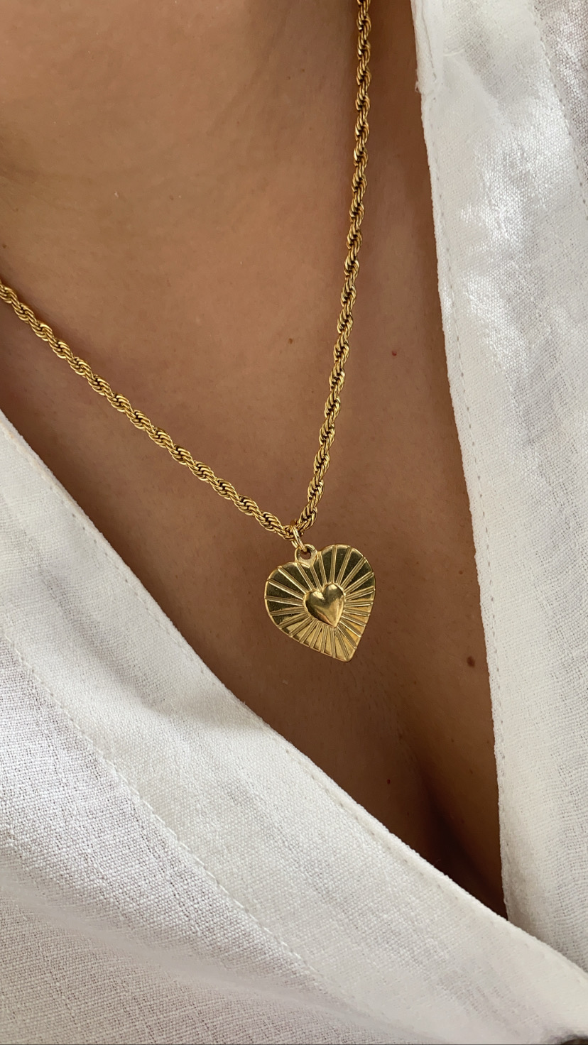 Colar dourado com pendente em forma de coração com relevo, sobre pele e camisa branca