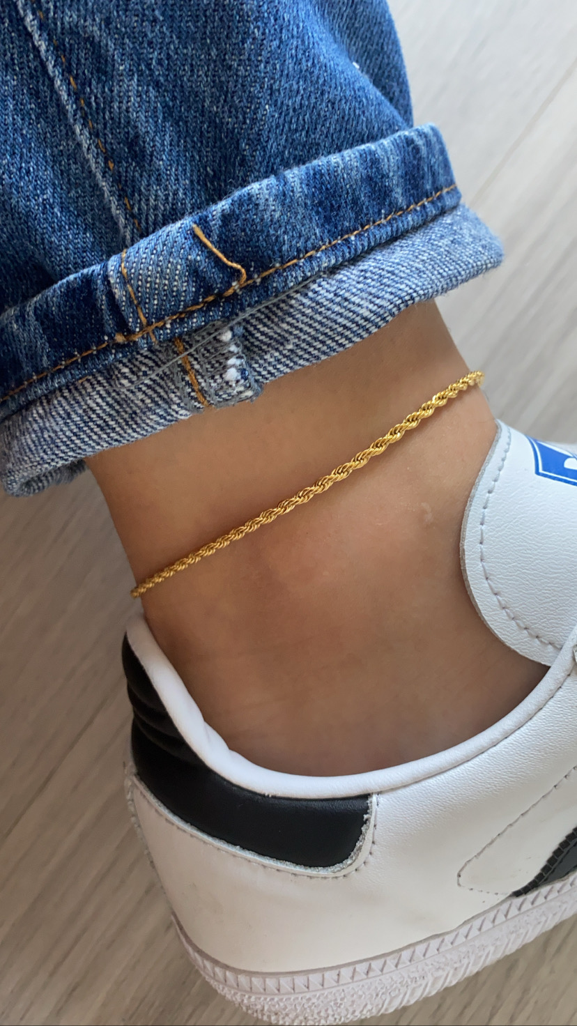 Tornozeleira dourada no tornozelo com jeans e ténis branco