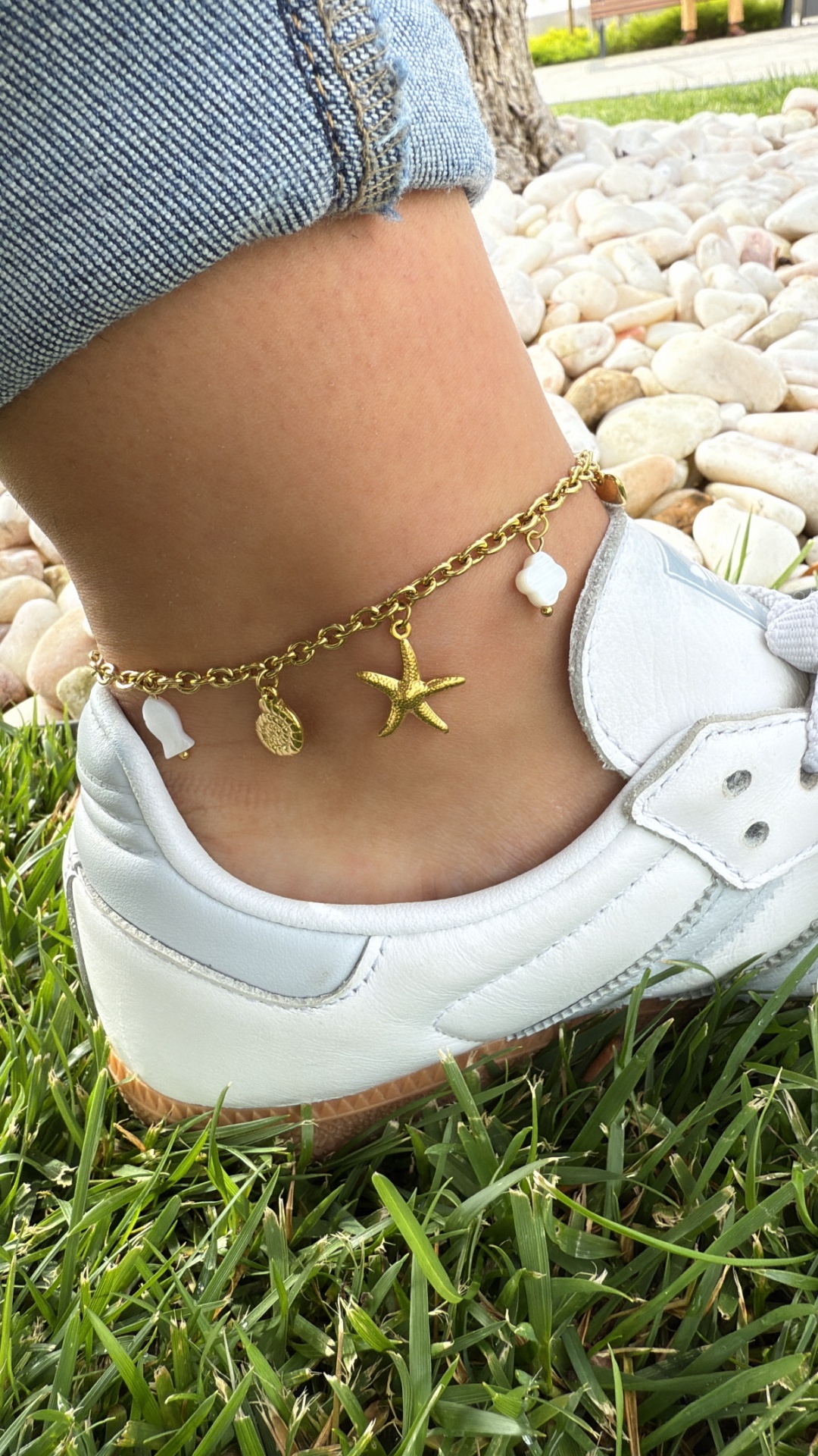 Tornozeleira dourada com pendentes de estrela do mar e conchas no tornozelo junto a sapato branco