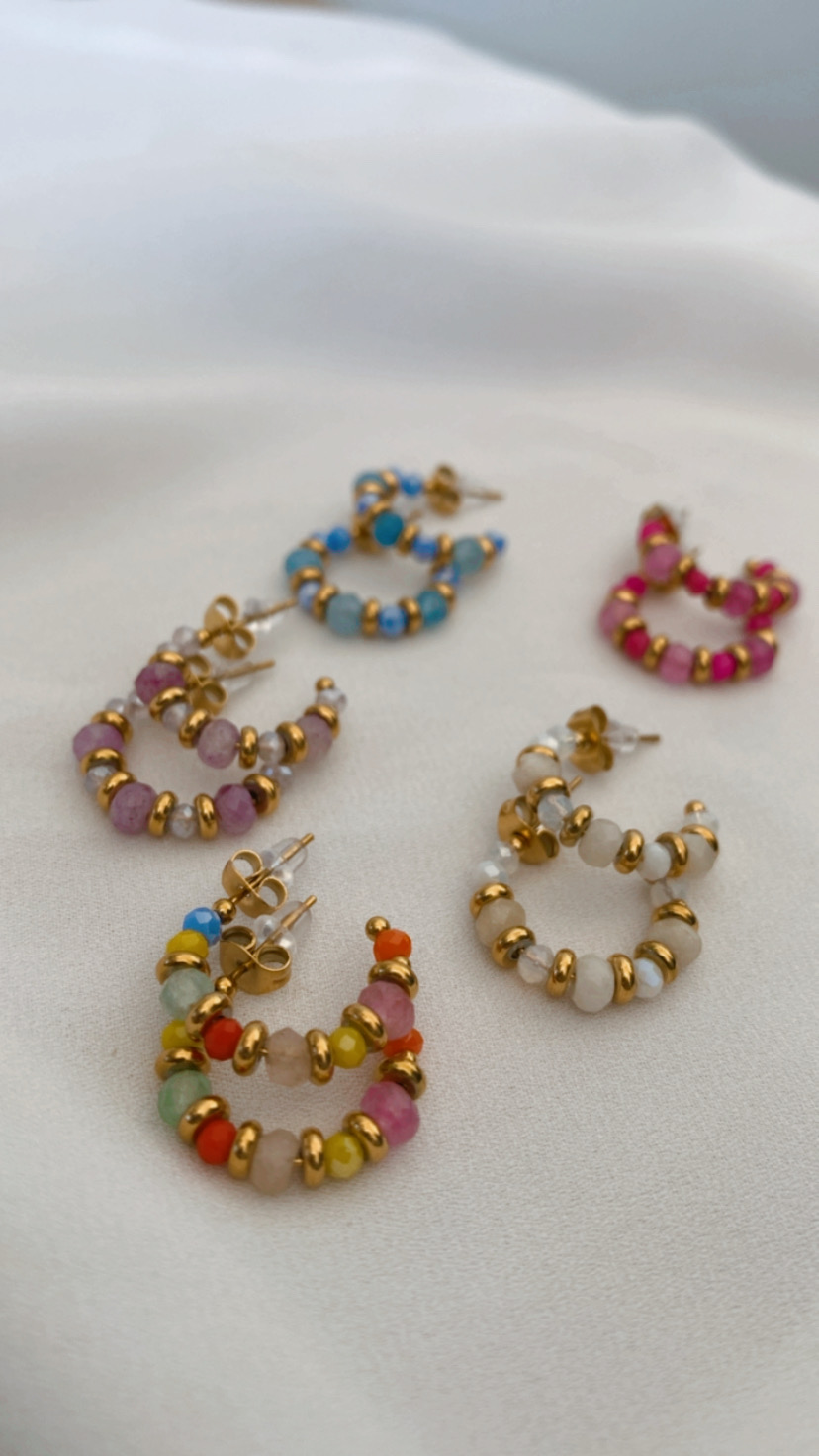 Seis pares de brincos coloridos em forma de argola sobre tecido branco.