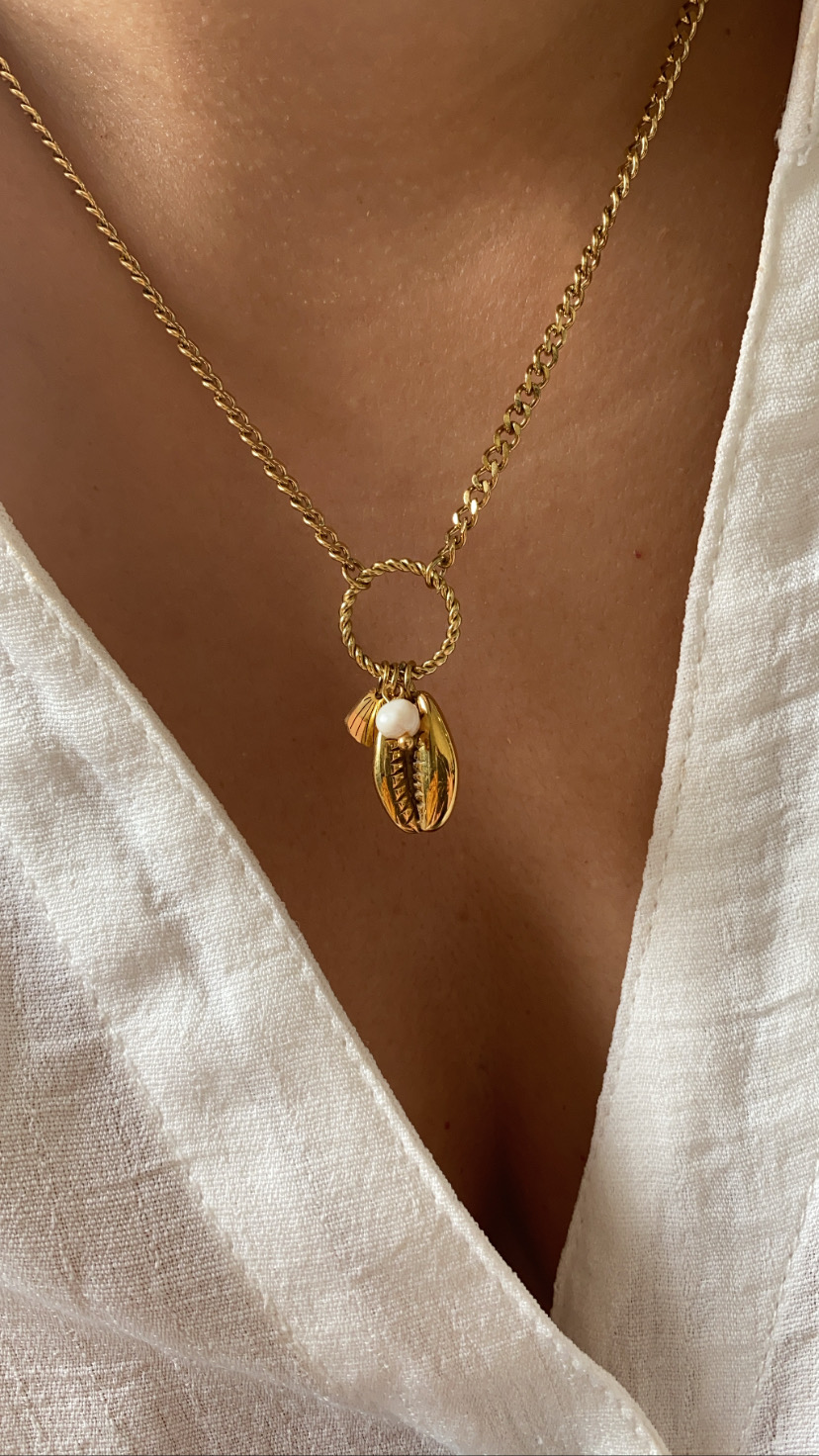 Colar dourado com pendente de conchas e pérola sobre camisa branca