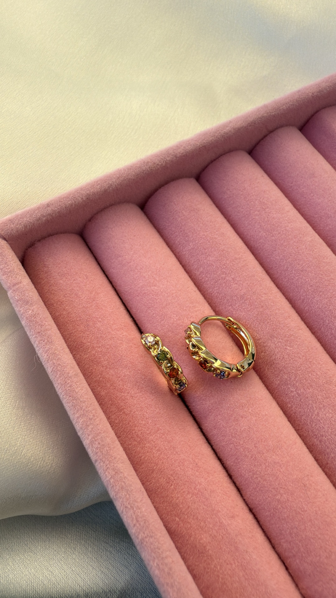 Brincos de argola dourados com pedras coloridas numa caixa rosa de veludo