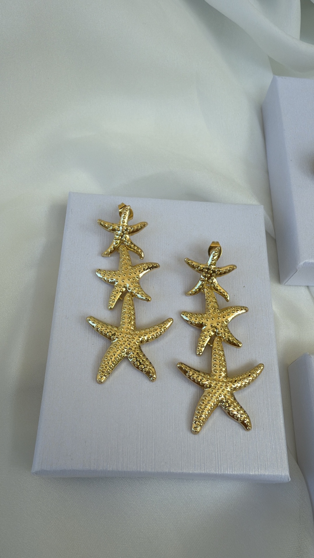 Brincos dourados em forma de estrelas do mar sobre caixa branca