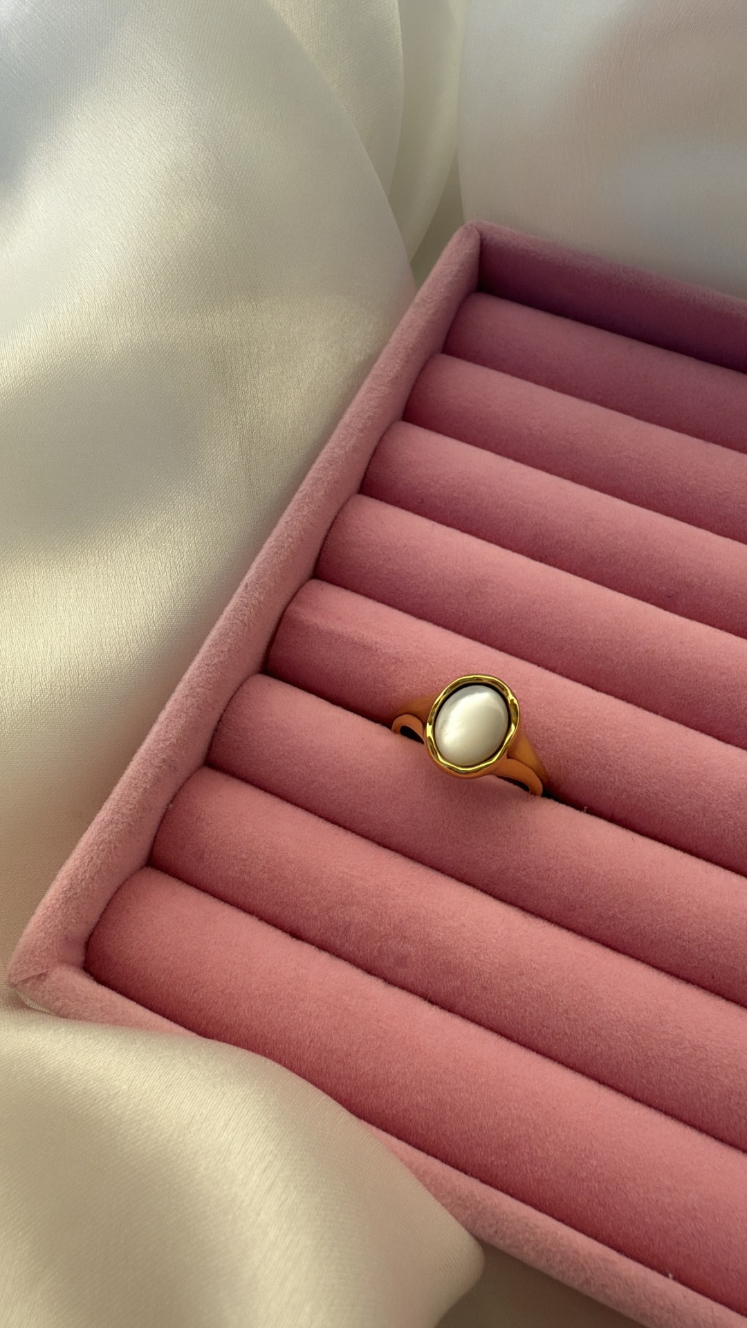 Anel dourado com pedra oval branca em caixa rosa acolchoada